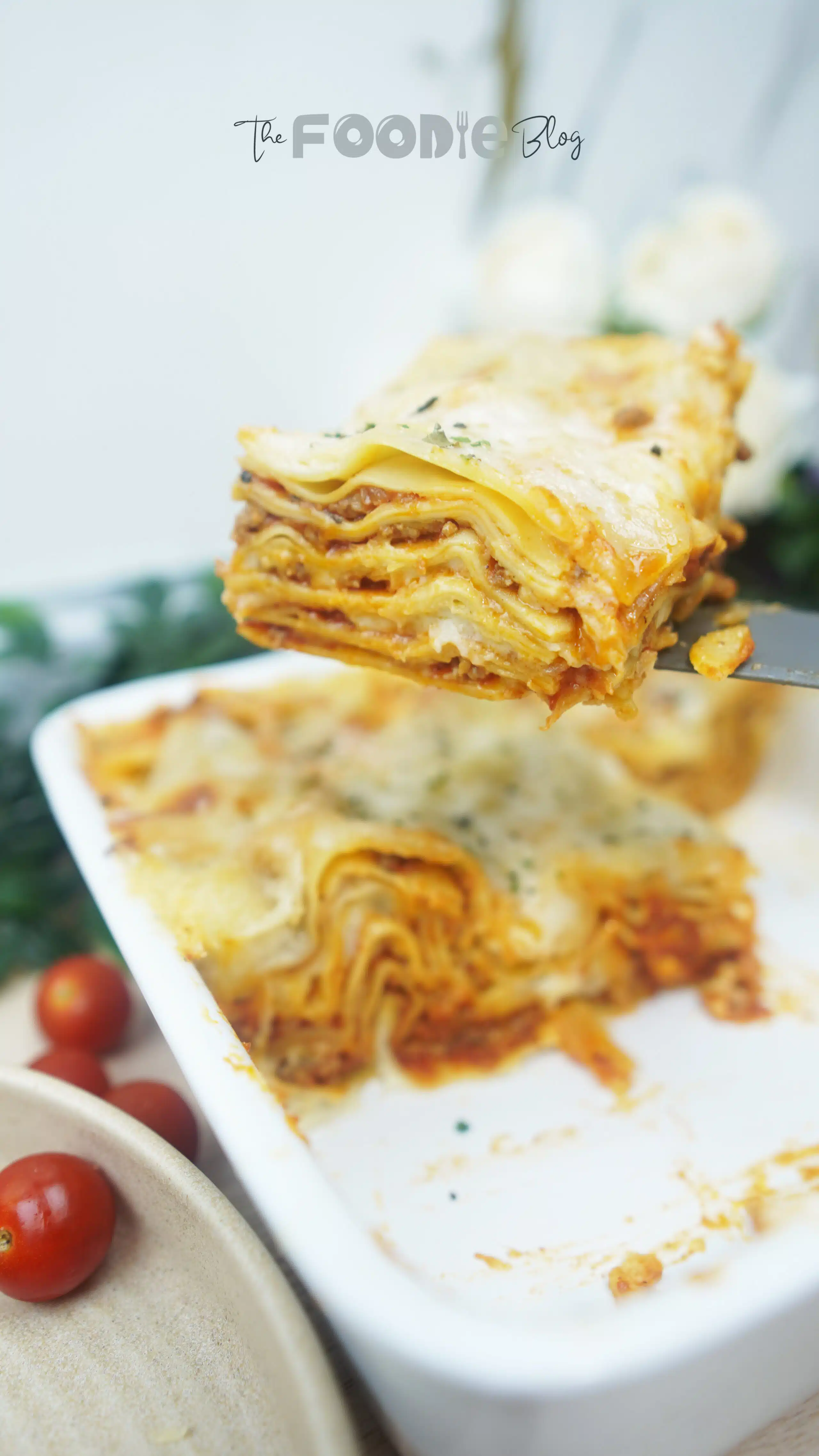 Close up of a tall slice of cheesy homemade meat lasagna being lifted from a white baking dish, showing all the sauce and pasta layers.