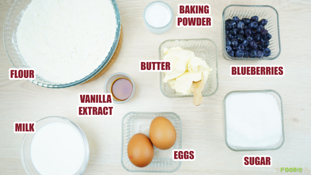 Labeled ingredients for blueberries cake including flour, sugar, eggs, milk, butter, baking powder, vanilla, and blueberries