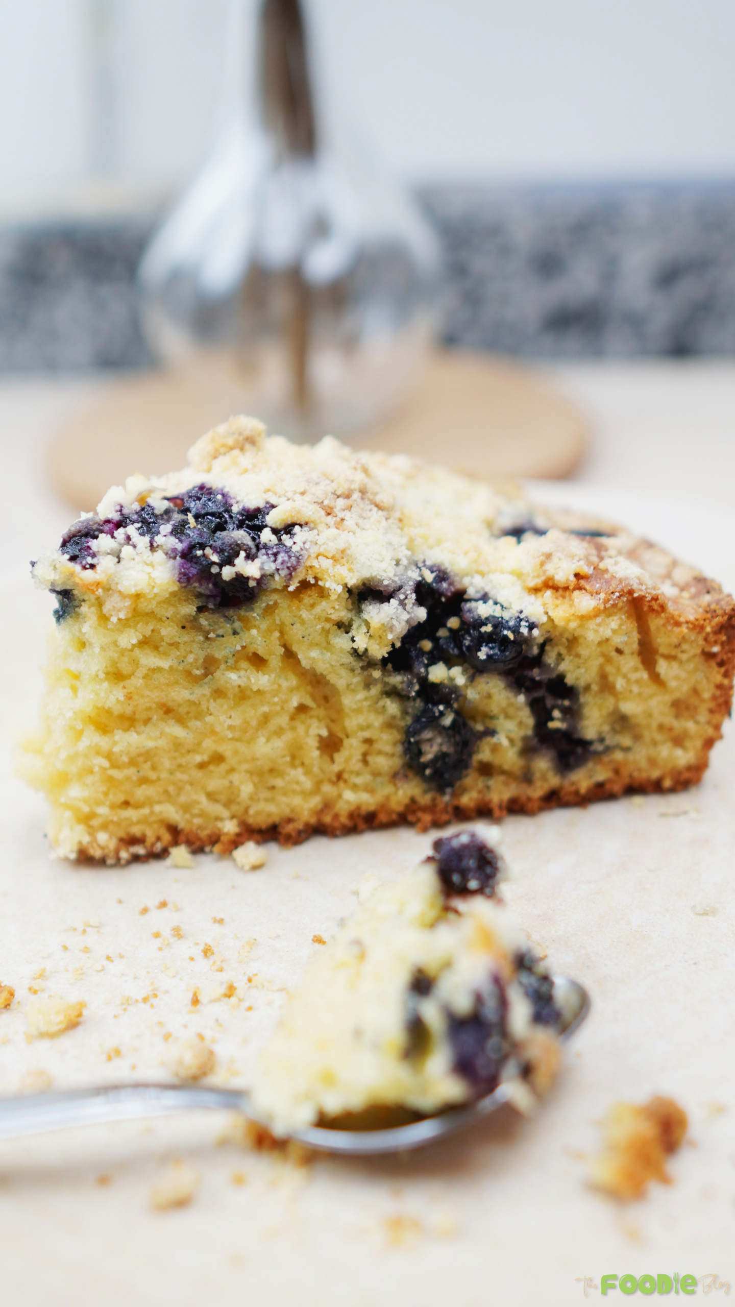 A slice of blueberries cake served on a white plate with crumb topping and blueberries
