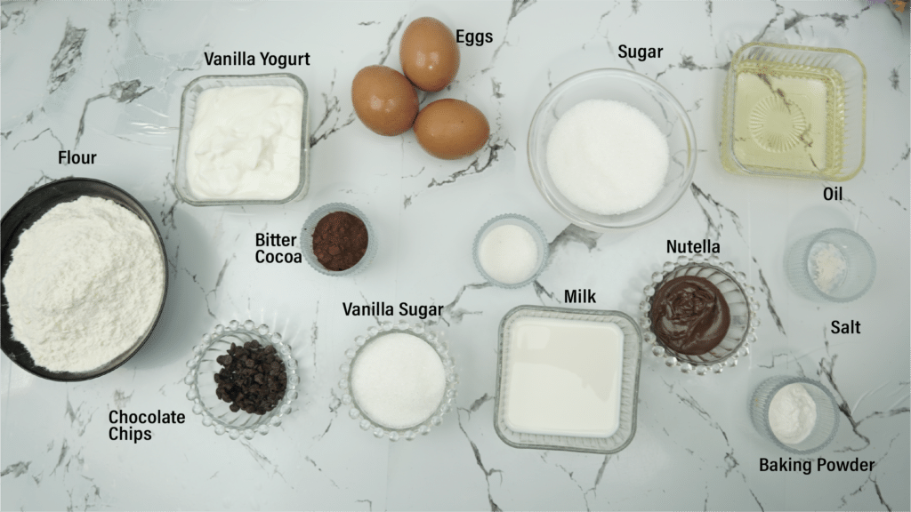 Ingredients for chocolate filled cake: flour, eggs, sugar, milk, oil, vanilla yogurt, Nutella, cocoa, baking powder, salt, and chocolate chips.