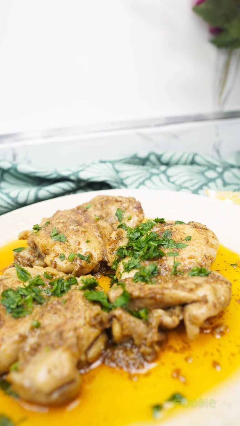 Close-up of cooked chicken thighs on a plate with golden butter sauce and chopped herbs