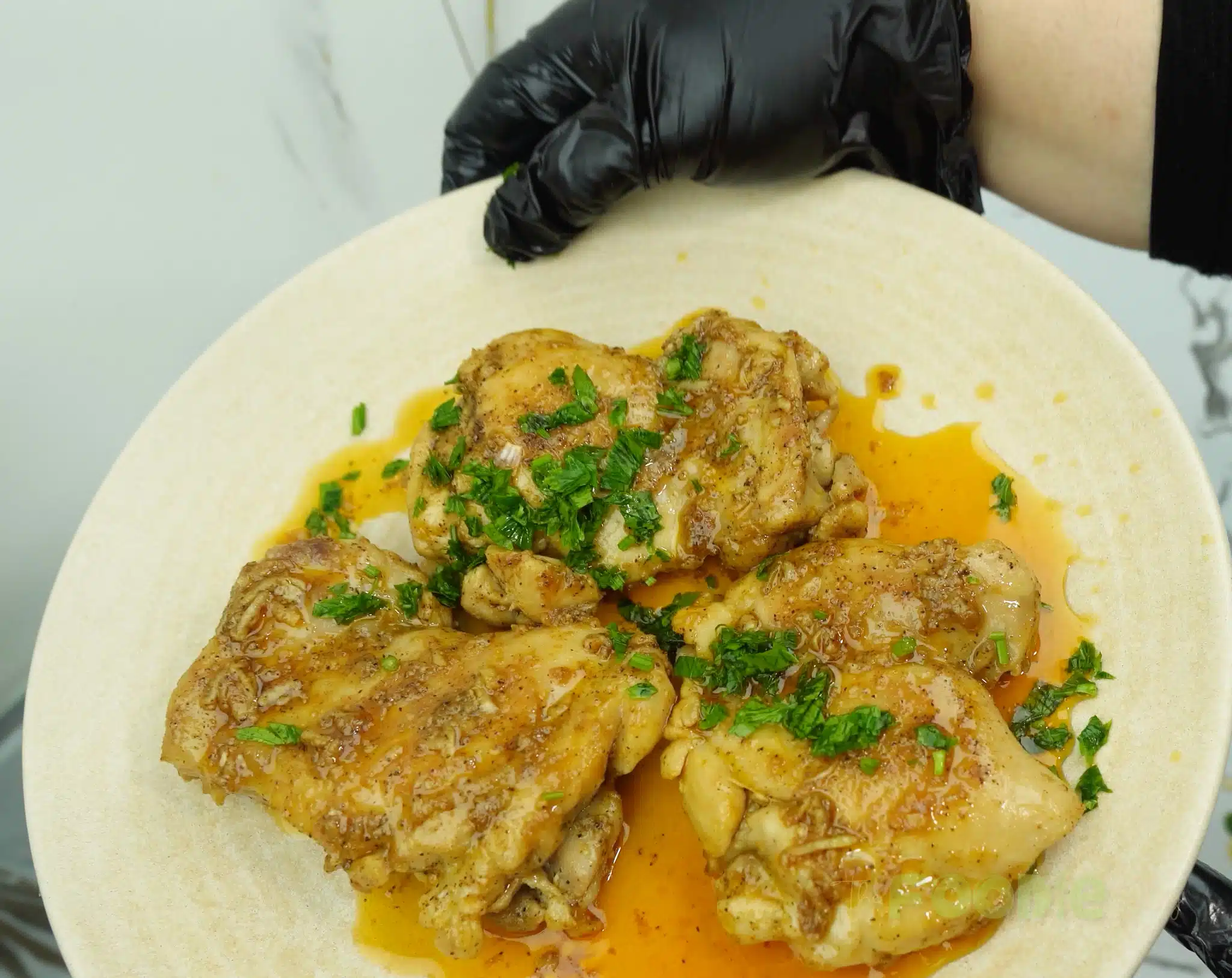 Plated garlic chicken thighs topped with chopped herbs and surrounded by buttery pan sauce