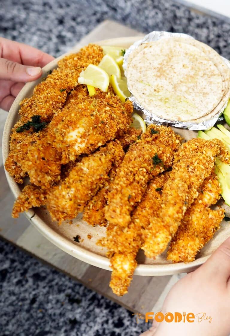 plate of crunchy chicken strips with tortillas, avocado slices, and lemon wedges