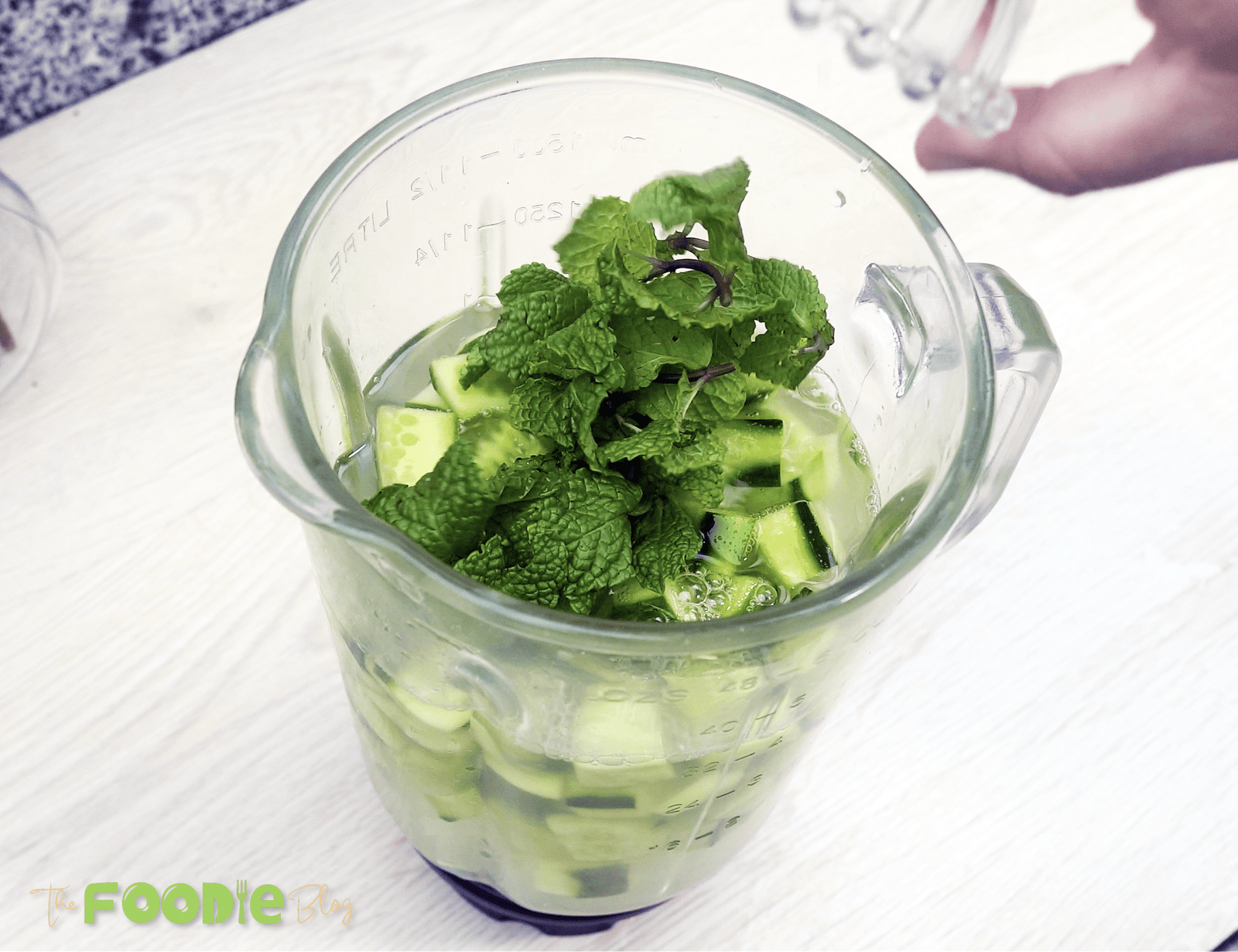 Blender jar filled with chopped cucumber, mint leaves, and water before blending