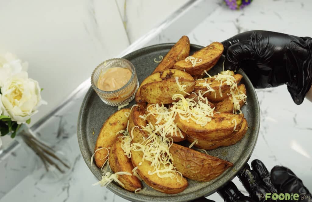 Plate of baked potato wedges topped with shredded cheese and a small bowl of sauce