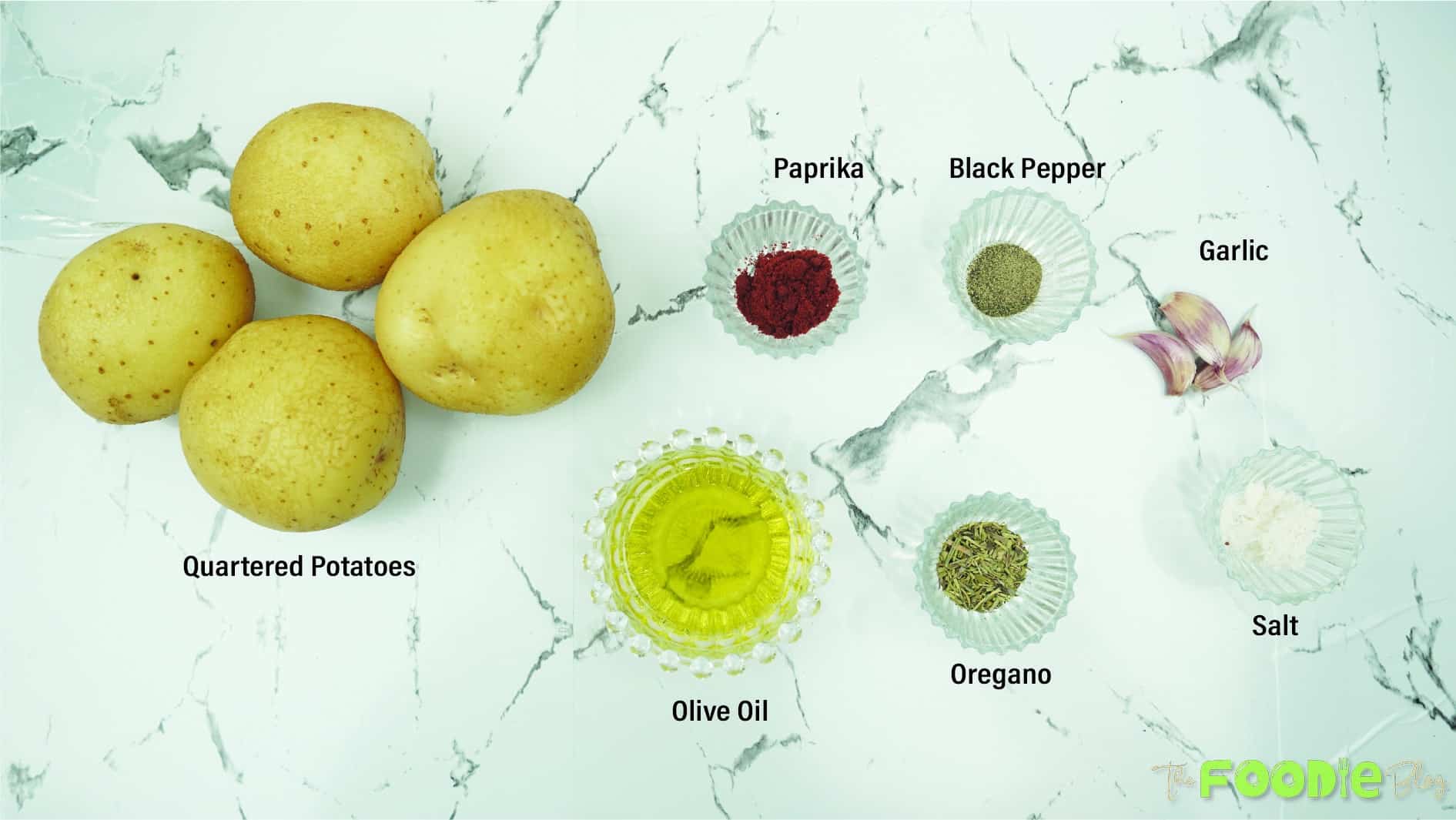 Ingredients for baked potato wedges arranged on a counter, including potatoes, olive oil, garlic, paprika, oregano, salt, and black pepper