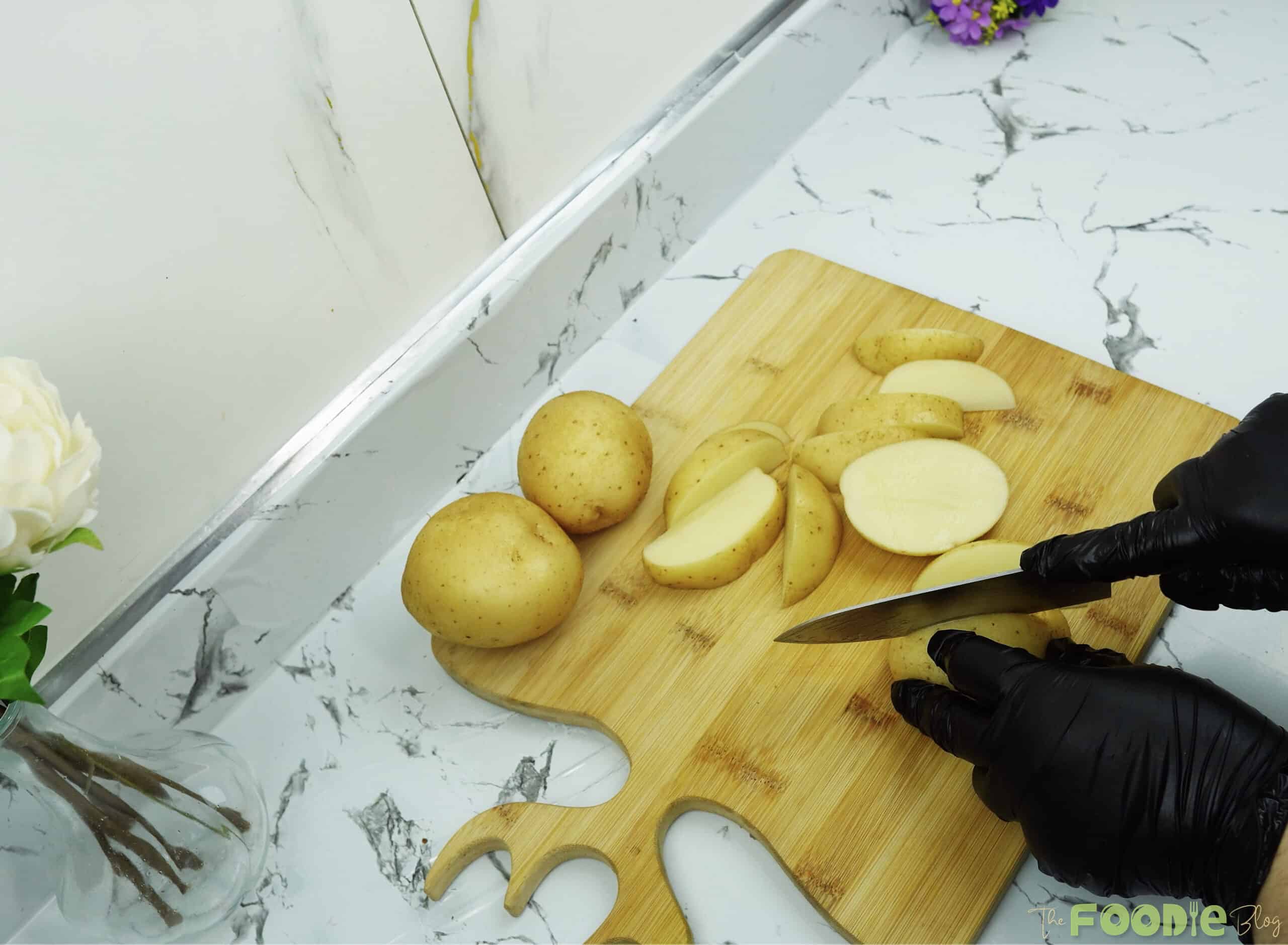 Hands slicing potatoes into wedges on a wooden cutting board
