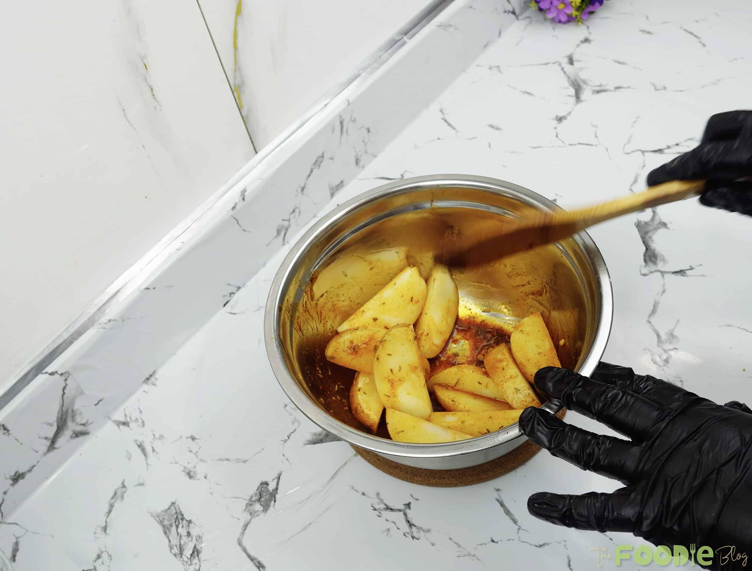 Potato wedges being tossed in a bowl with seasoned oil