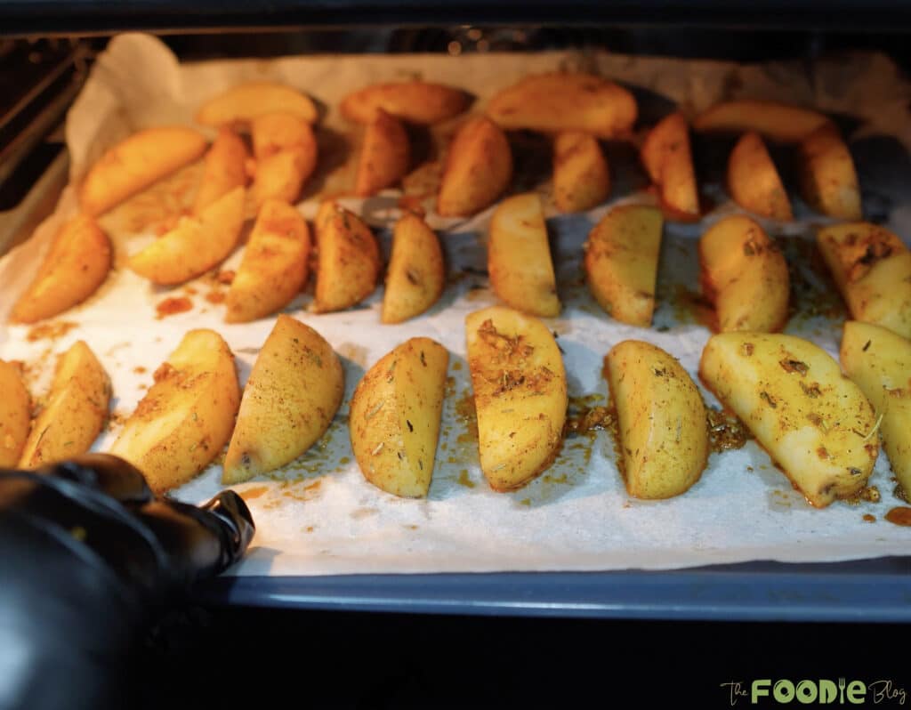 Potato wedges roasting on a baking sheet inside the oven