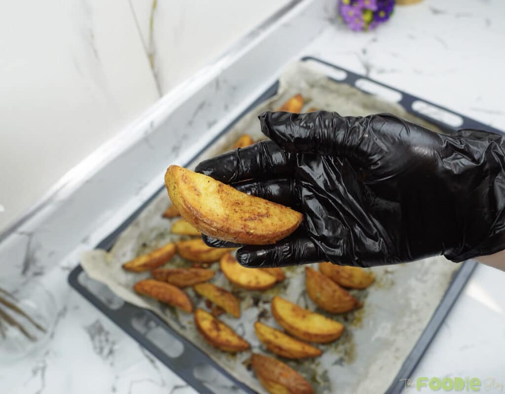 A baked potato wedge held up close showing a golden, crispy exterior