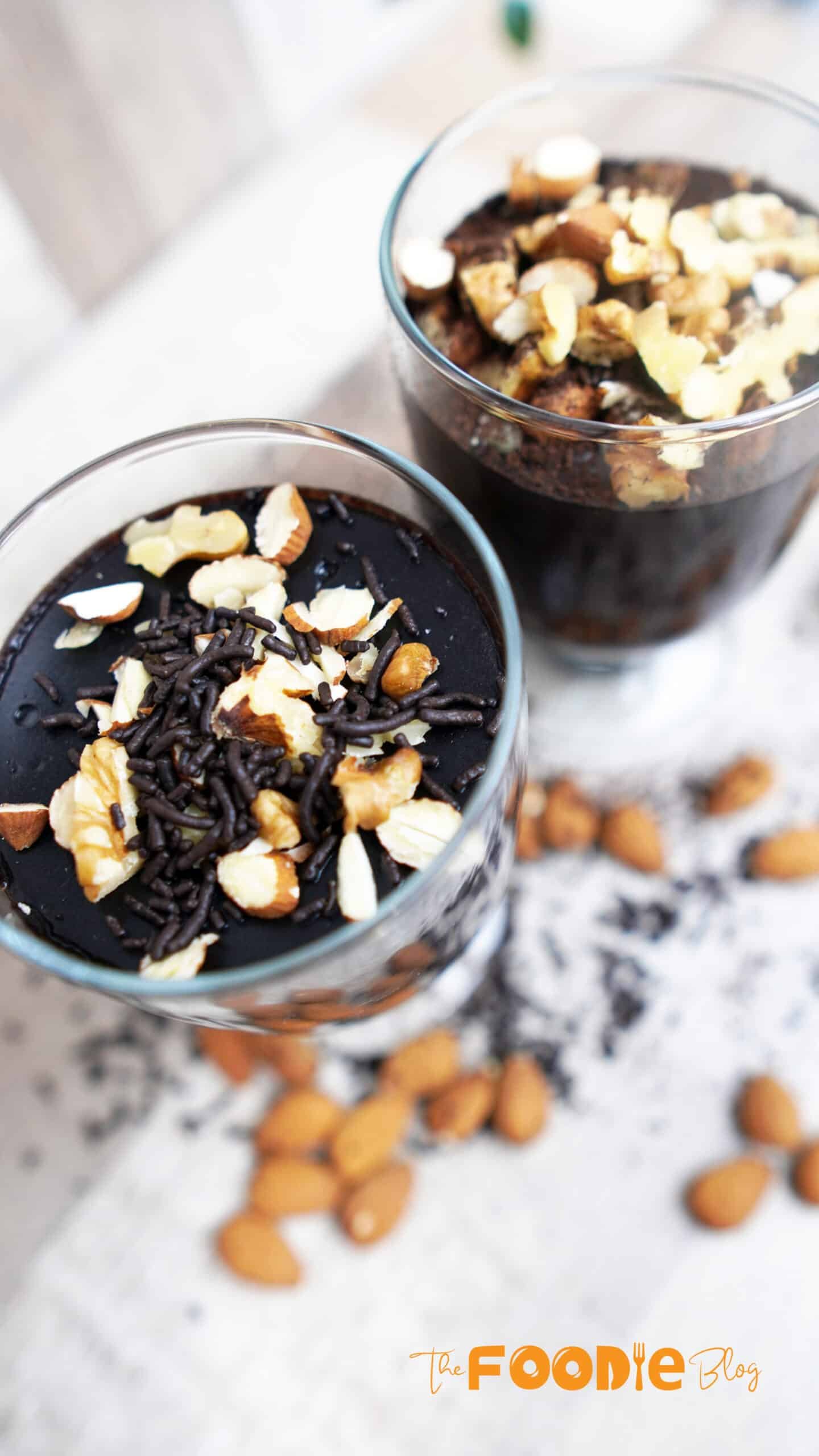 Three finished chocolate pudding cups on a wooden board with a spoon nearby.