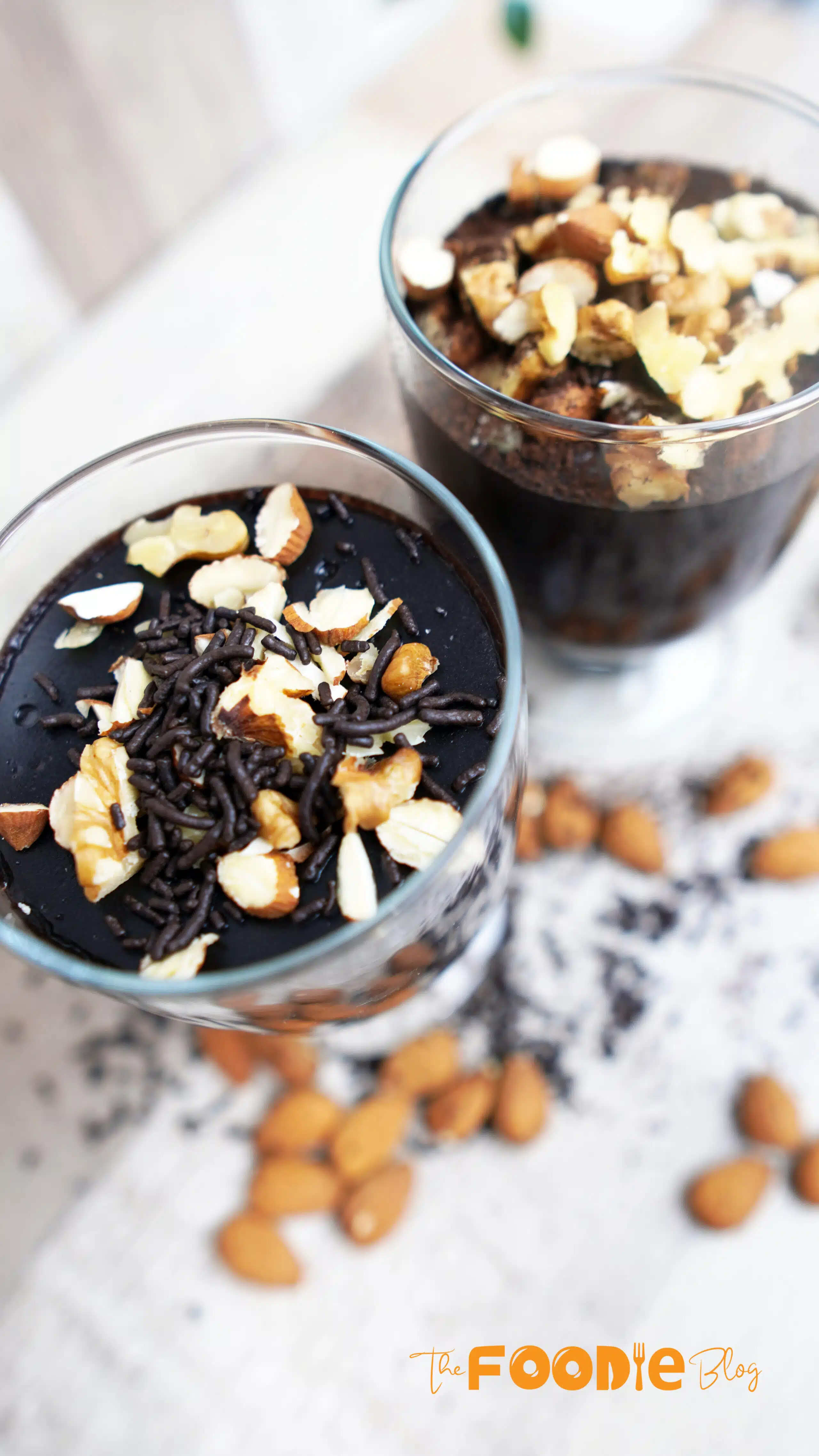 Three finished chocolate pudding cups on a wooden board with a spoon nearby.