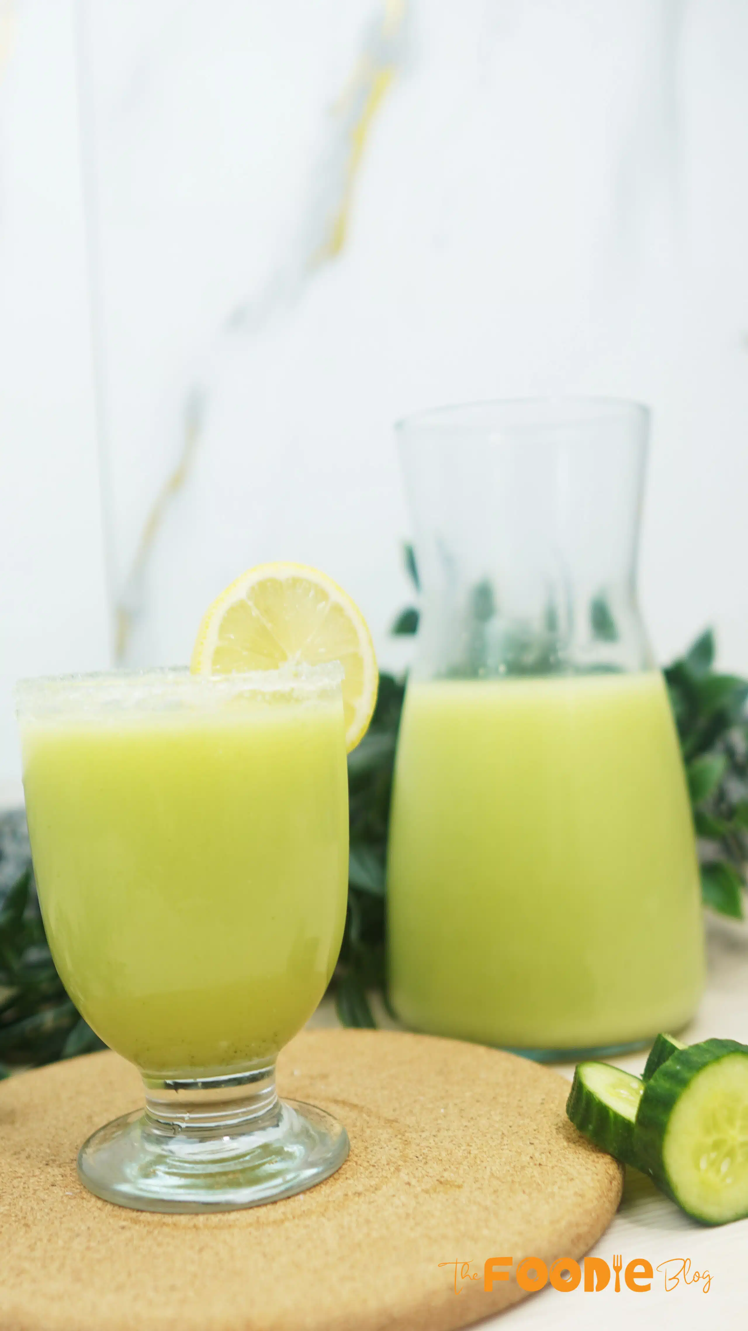 Glass of pale-green cucumber lemonade on a board with cucumber slices nearby