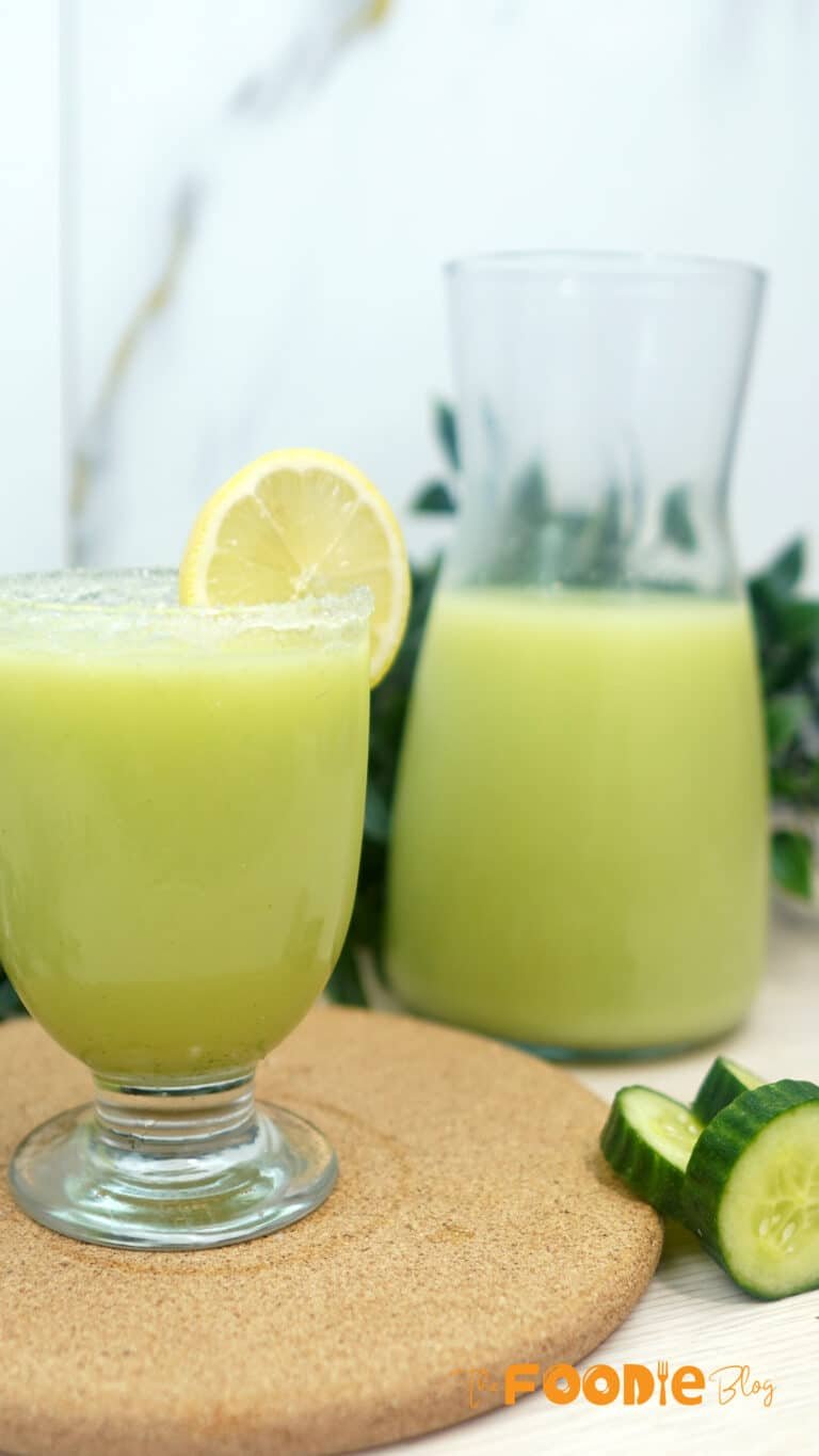 Creamy cucumber lemonade in a glass with a lemon slice garnish and a pitcher in the background