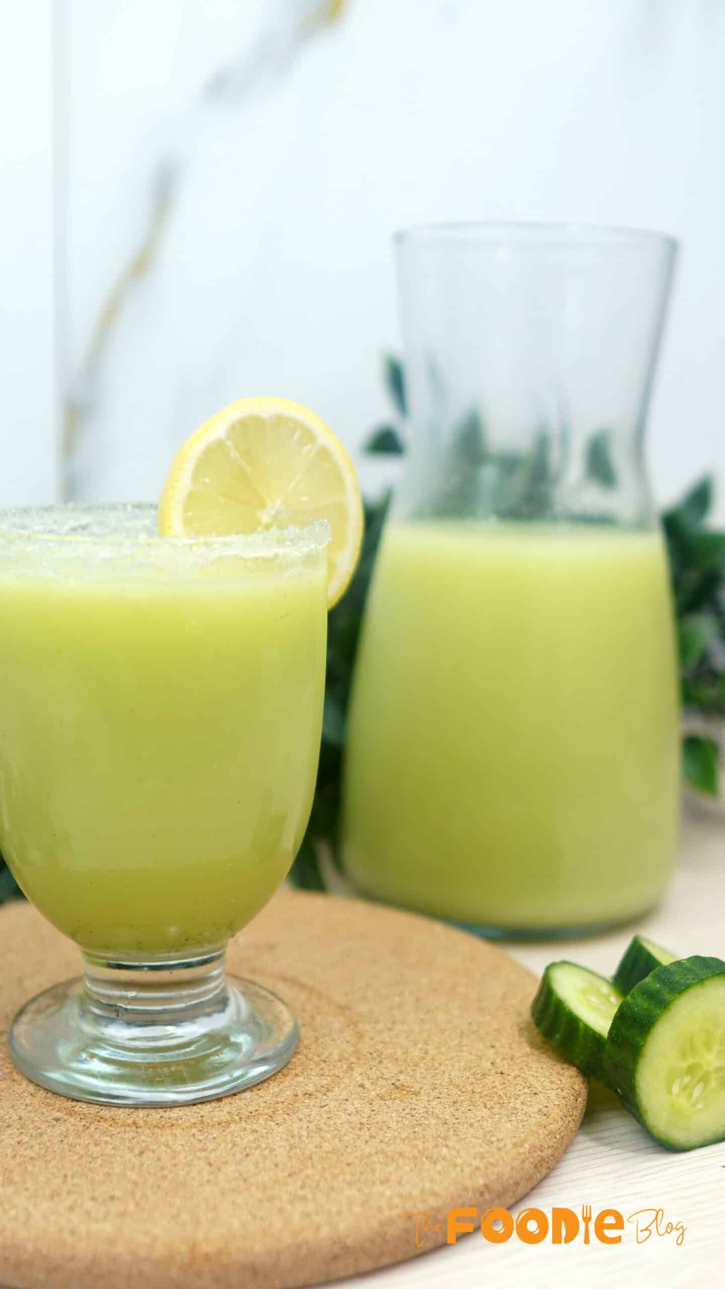 Creamy cucumber lemonade in a glass with a lemon slice garnish and a pitcher in the background