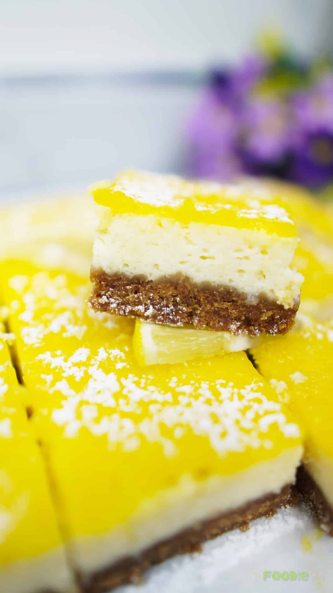 Close-up of a lemon cheesecake bar held above the pan showing creamy center and lemon topping