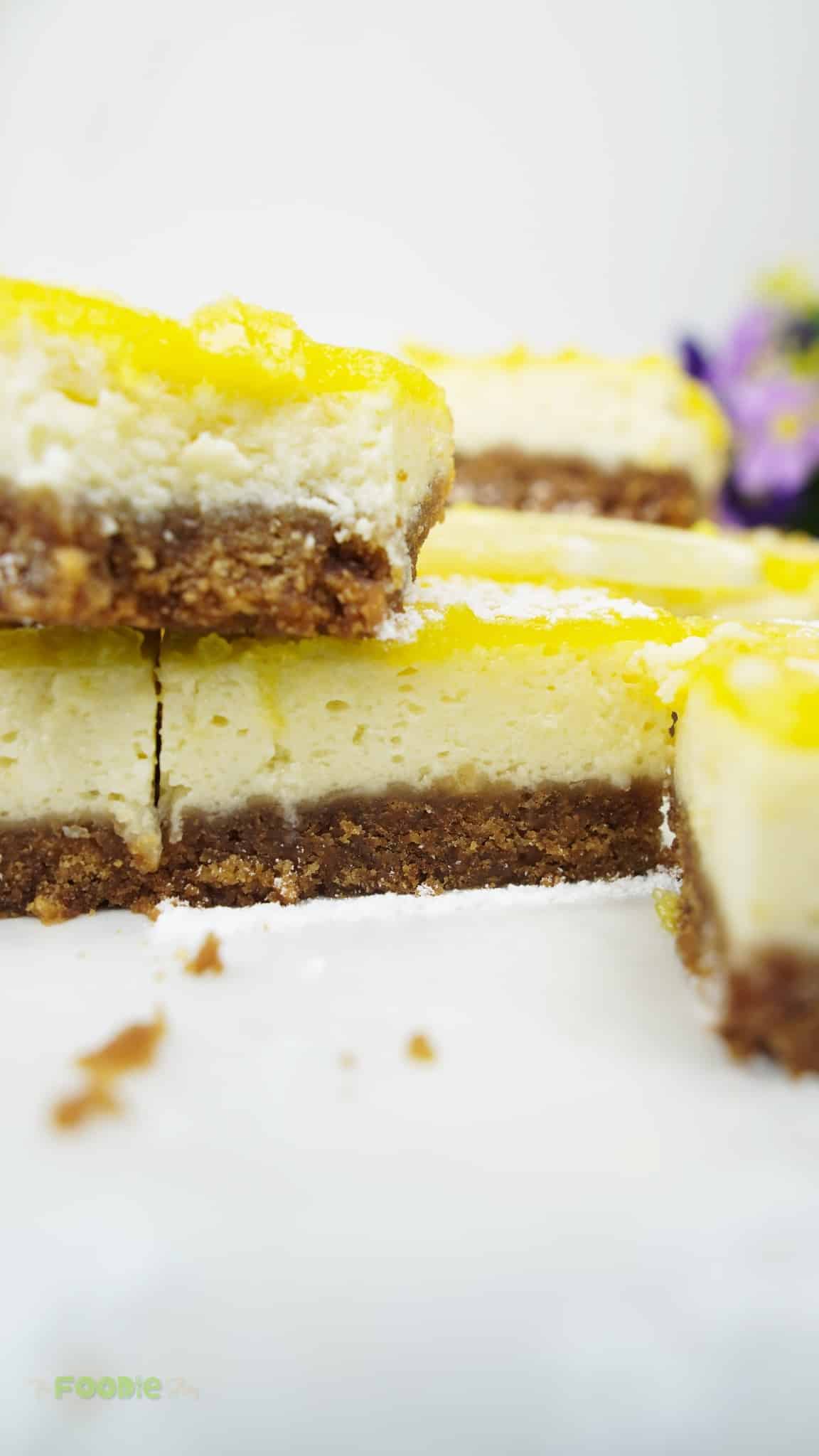 Cutting lemon cheesecake bars into squares and dusting with powdered sugar with lemon slices on top