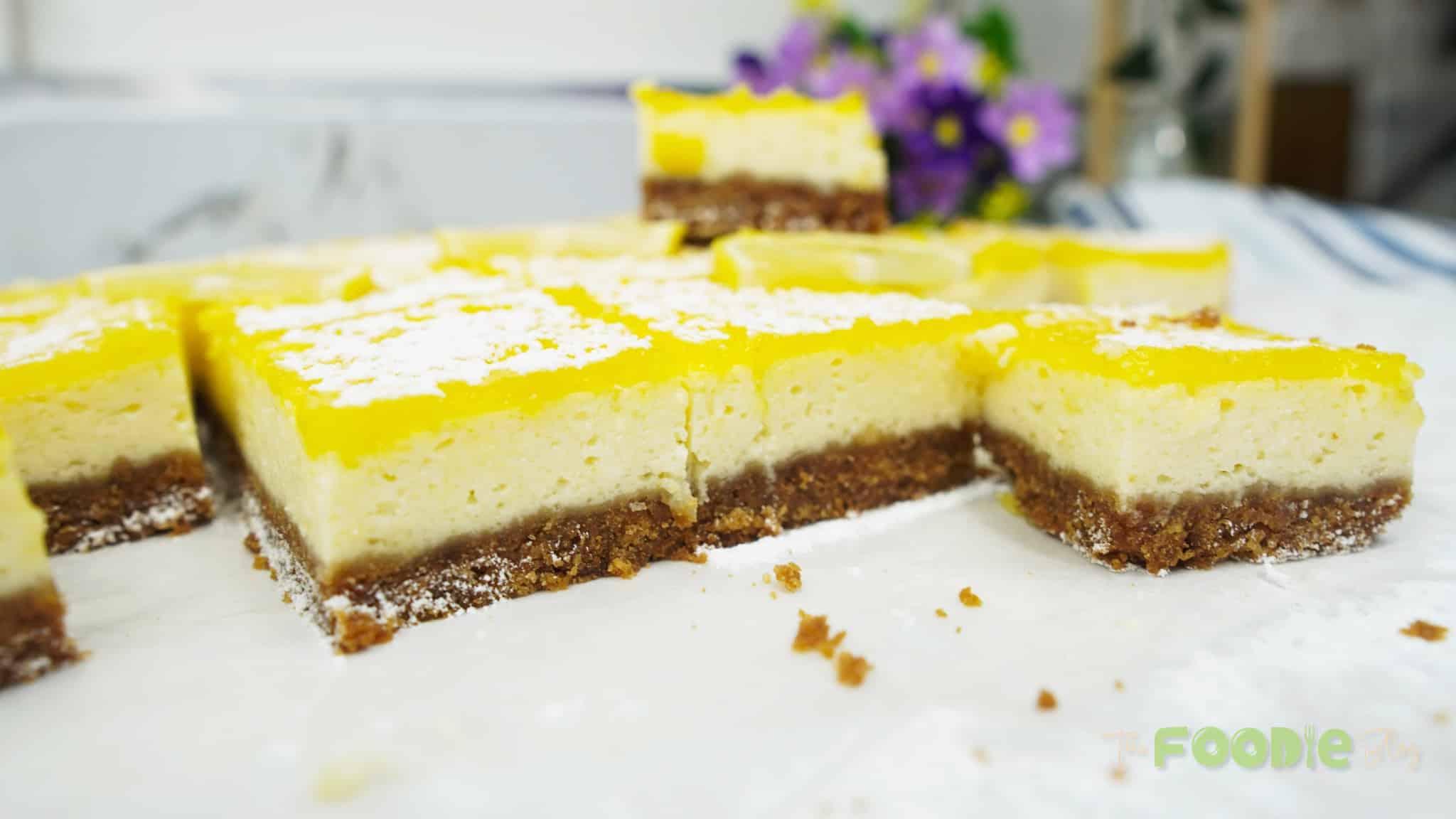 Lemon cheesecake bars with a cookie crust and bright yellow lemon topping sliced on parchment paper