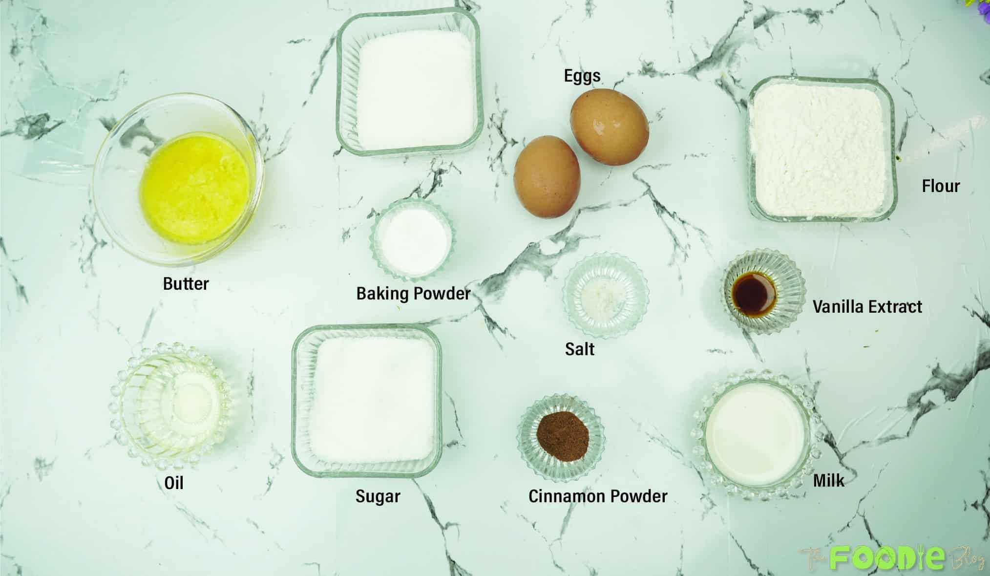 Ingredients laid out for mini cinnamon muffins including flour, eggs, butter, milk, vanilla, and cinnamon