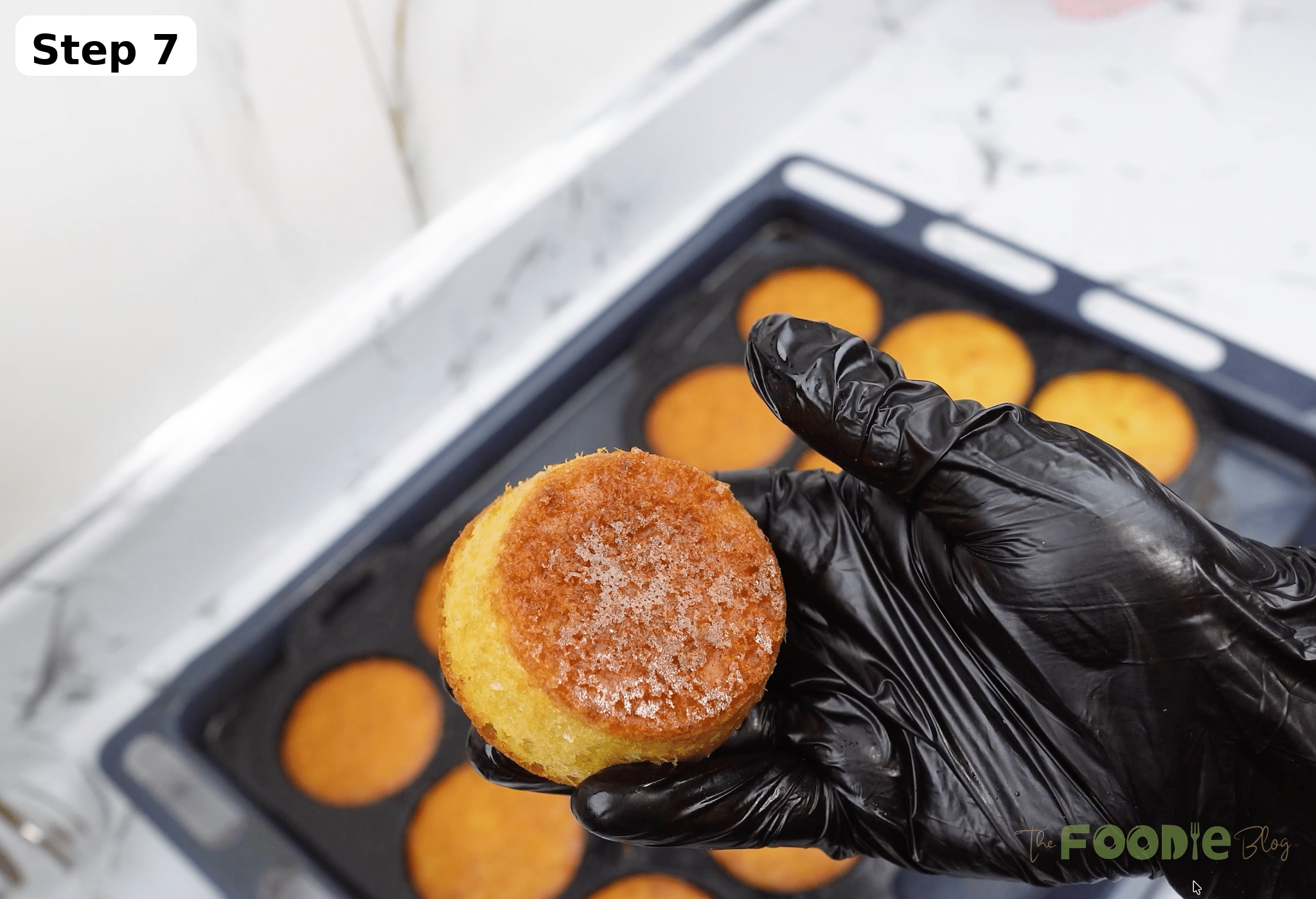 Hand holding a baked mini muffin with a tray of muffins in the background