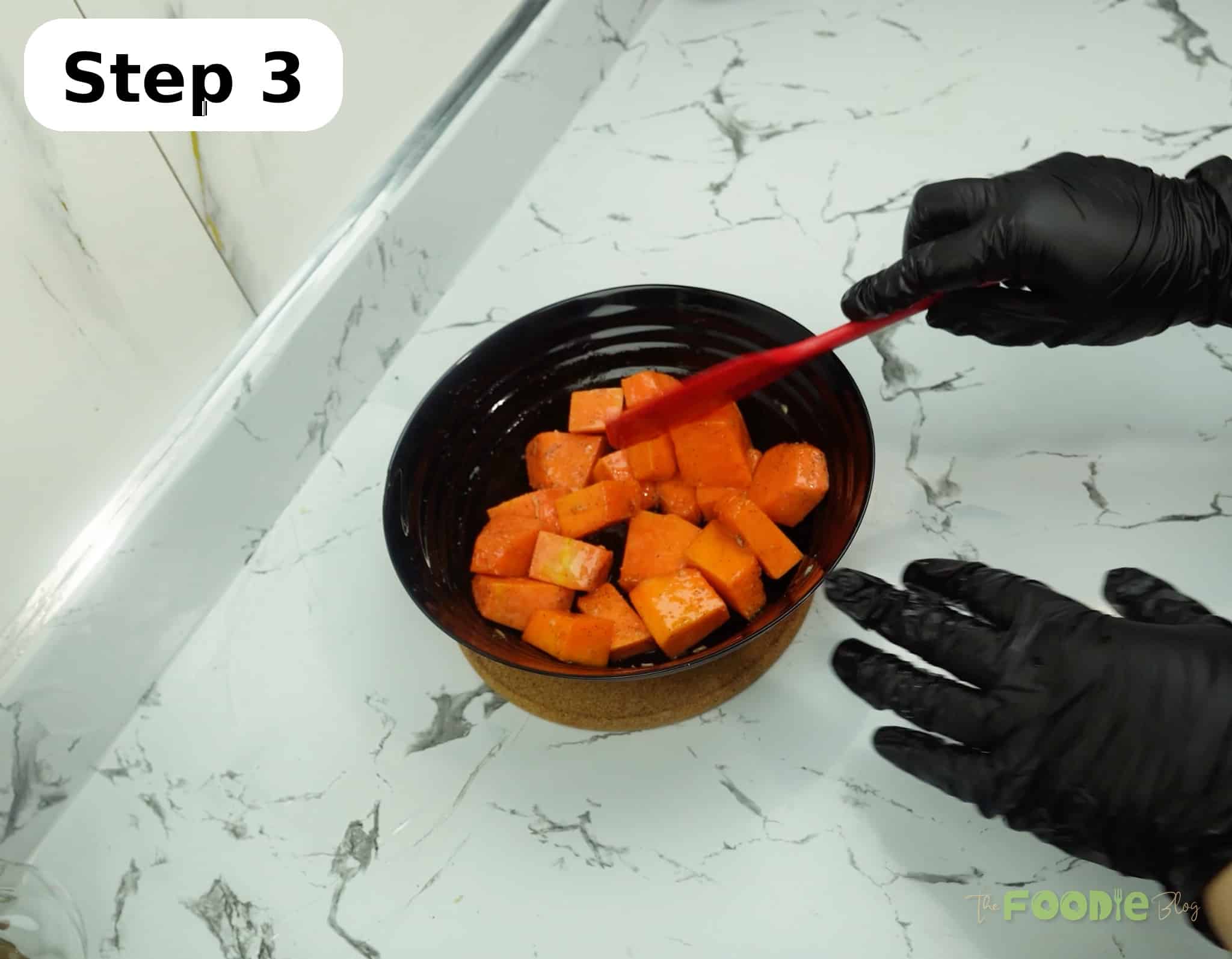 Pumpkin cubes in a bowl being tossed with seasoning using a red spatula