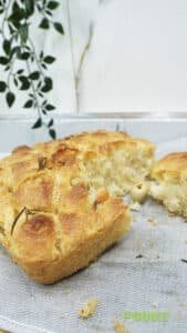 Sliced homemade olive and rosemary focaccia bread on a linen cloth with an airy crumb