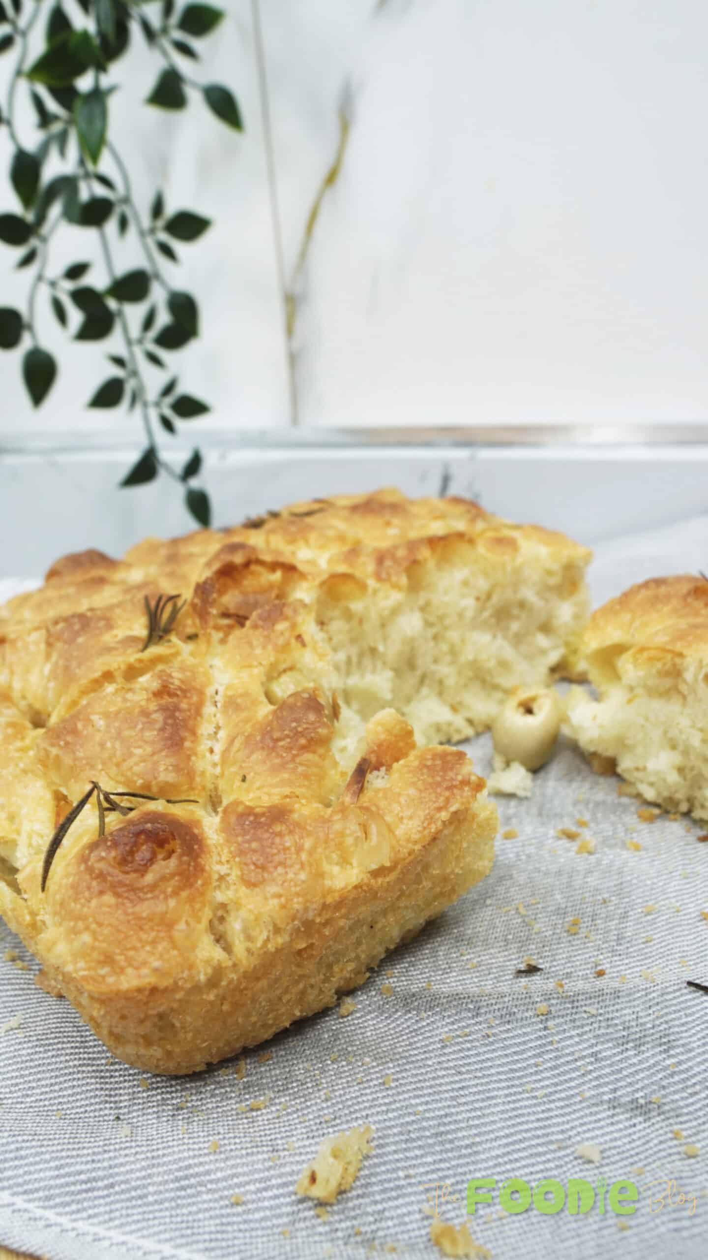 Sliced homemade olive and rosemary focaccia bread on a linen cloth with an airy crumb