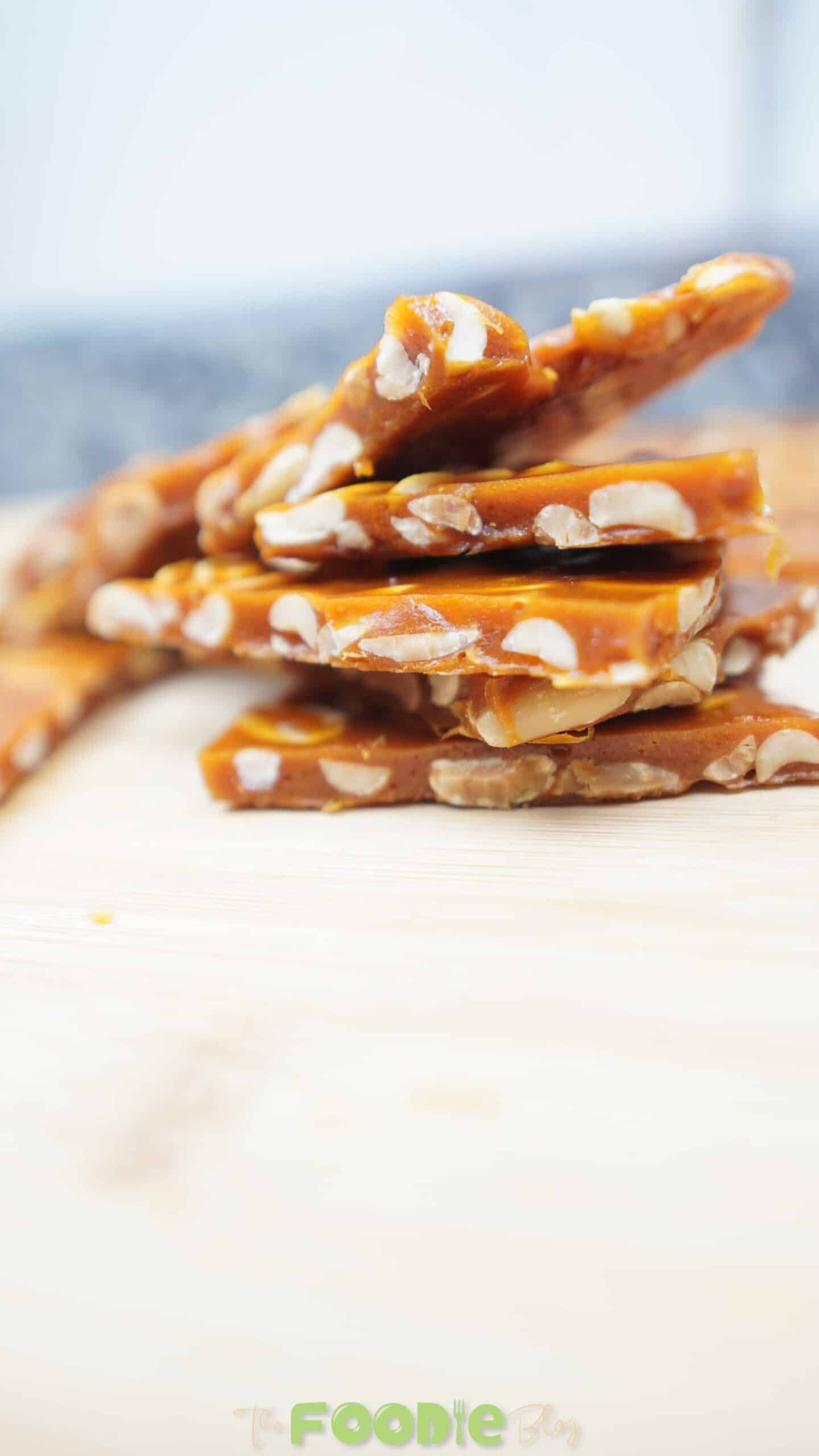 Peanut brittle pieces stacked on a cutting board with a bright, glossy caramel finish