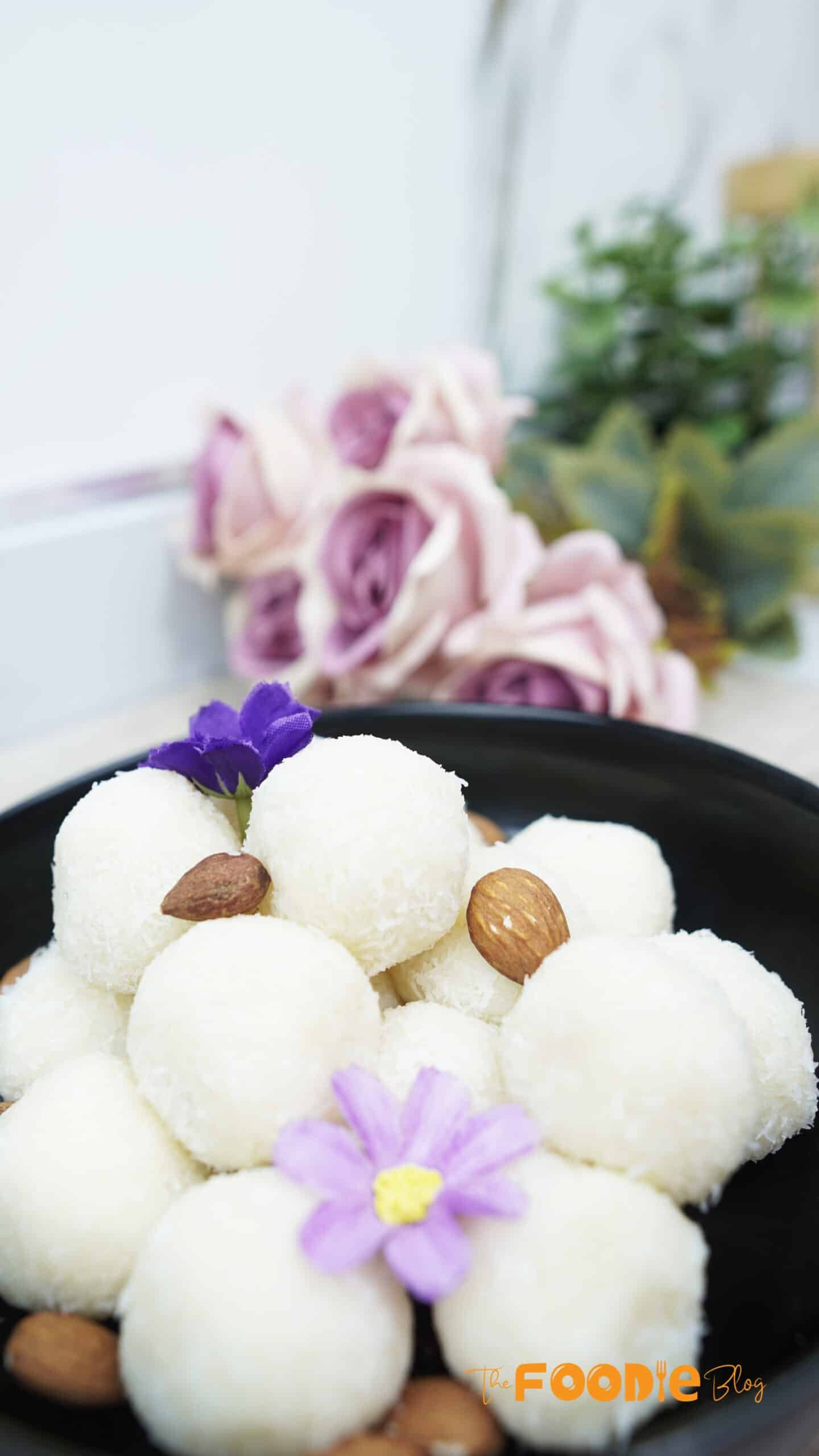 Finished coconut balls with almonds and flowers in the background