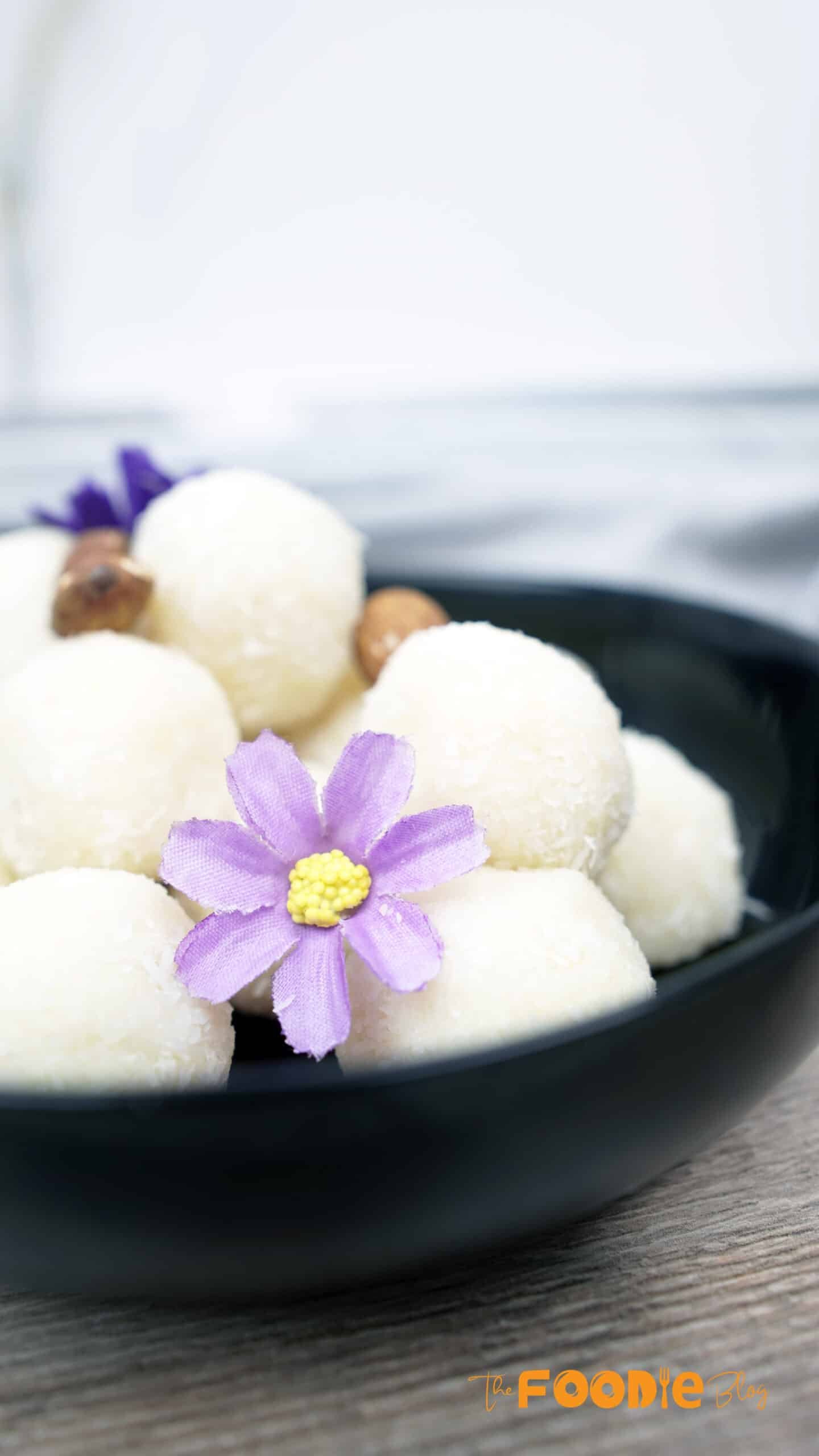 Coconut balls arranged in a black bowl with a purple flower on top