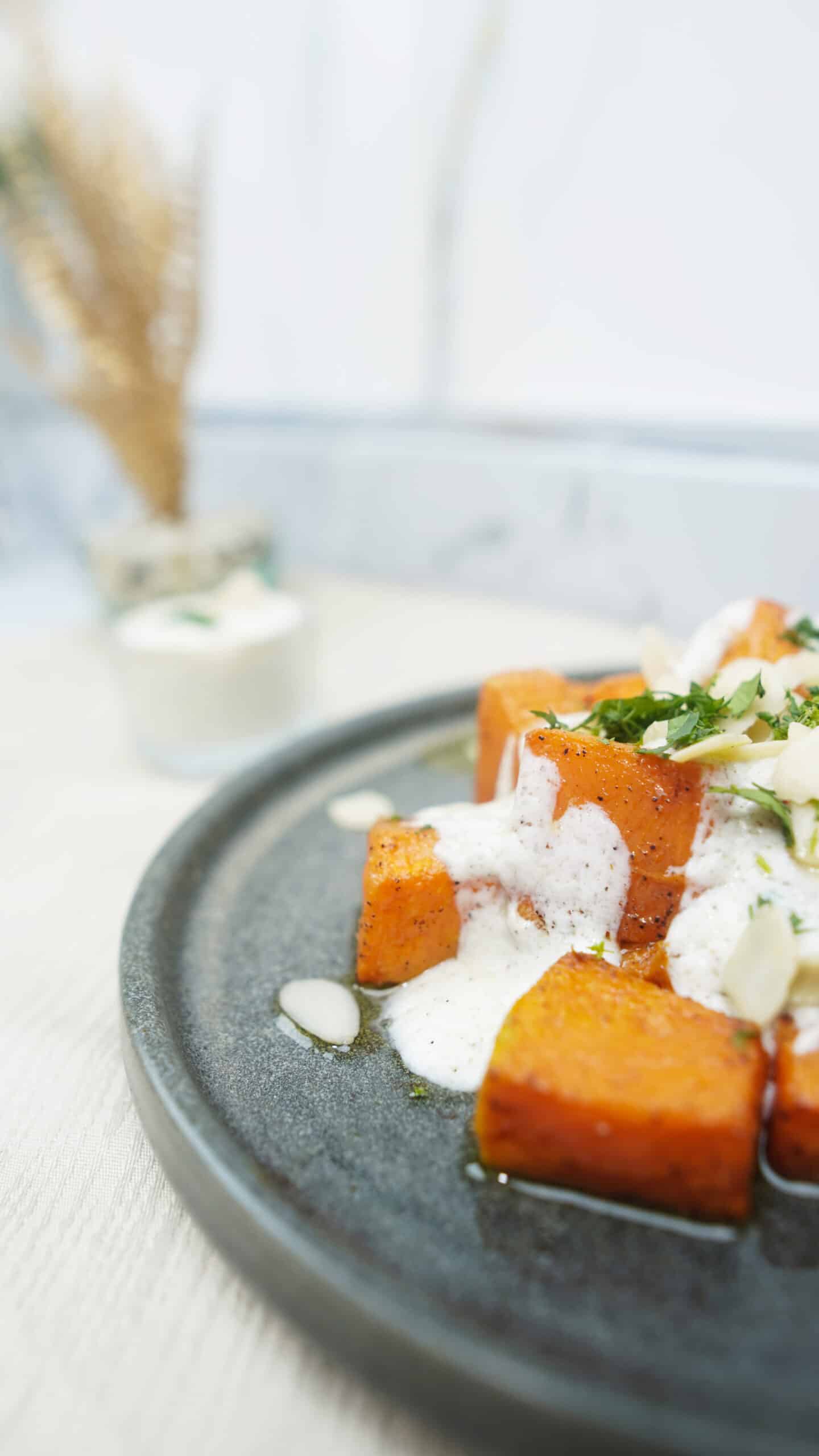 Close-up of roasted pumpkin with creamy yogurt sauce and sliced almonds on a plate