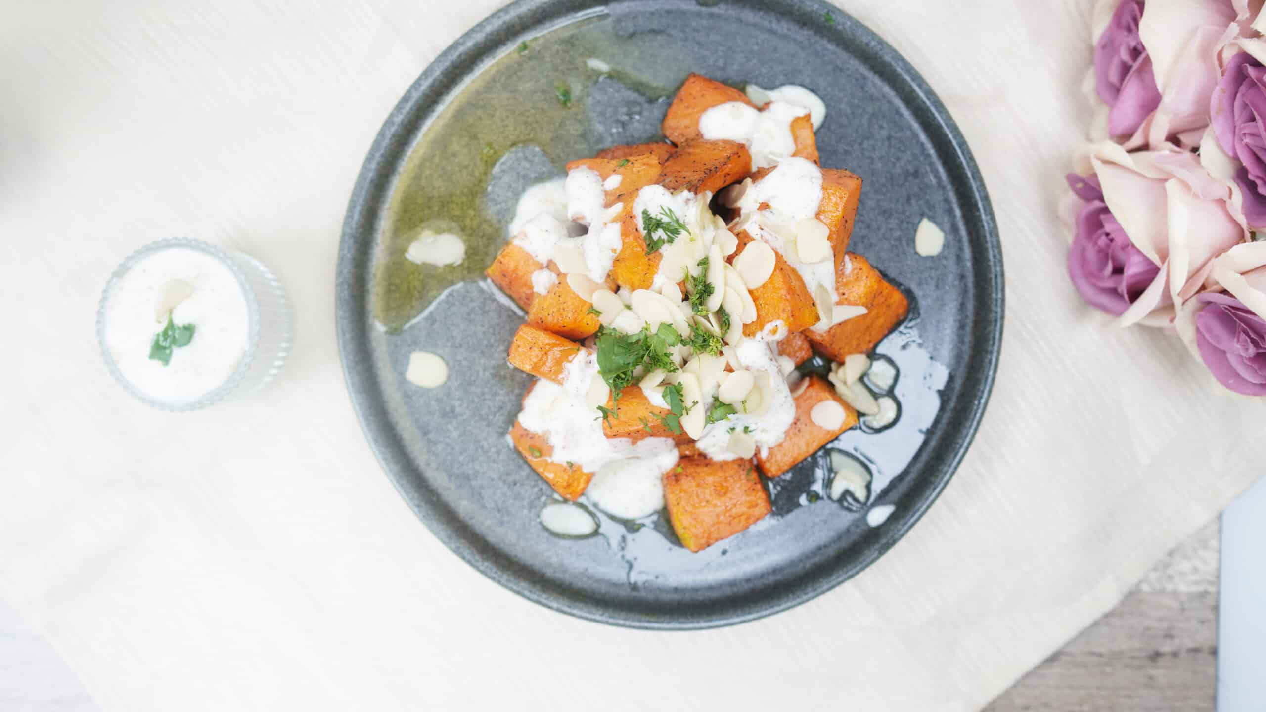 : Overhead view of plated roasted pumpkin topped with yogurt sauce, herbs, and almonds