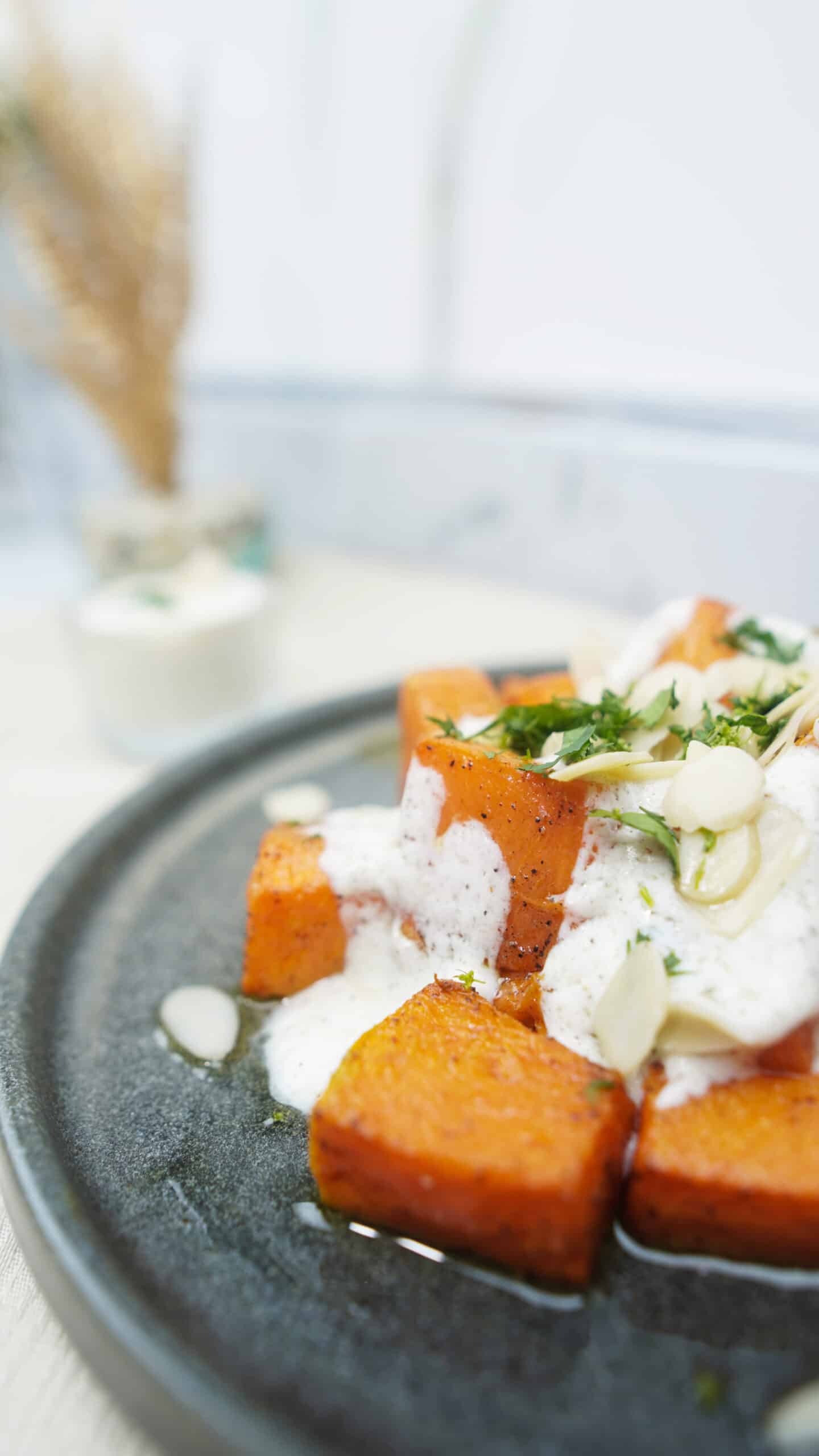Side-angle photo of roasted pumpkin with yogurt sauce and almonds, with a soft blurred background