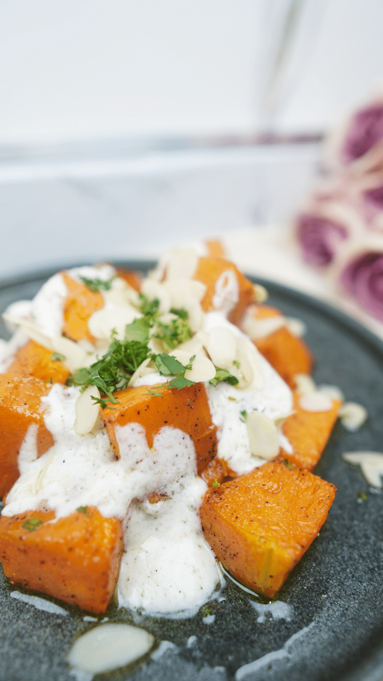 Roasted pumpkin cubes topped with lemon yogurt sauce, almonds, and parsley on a gray plate
