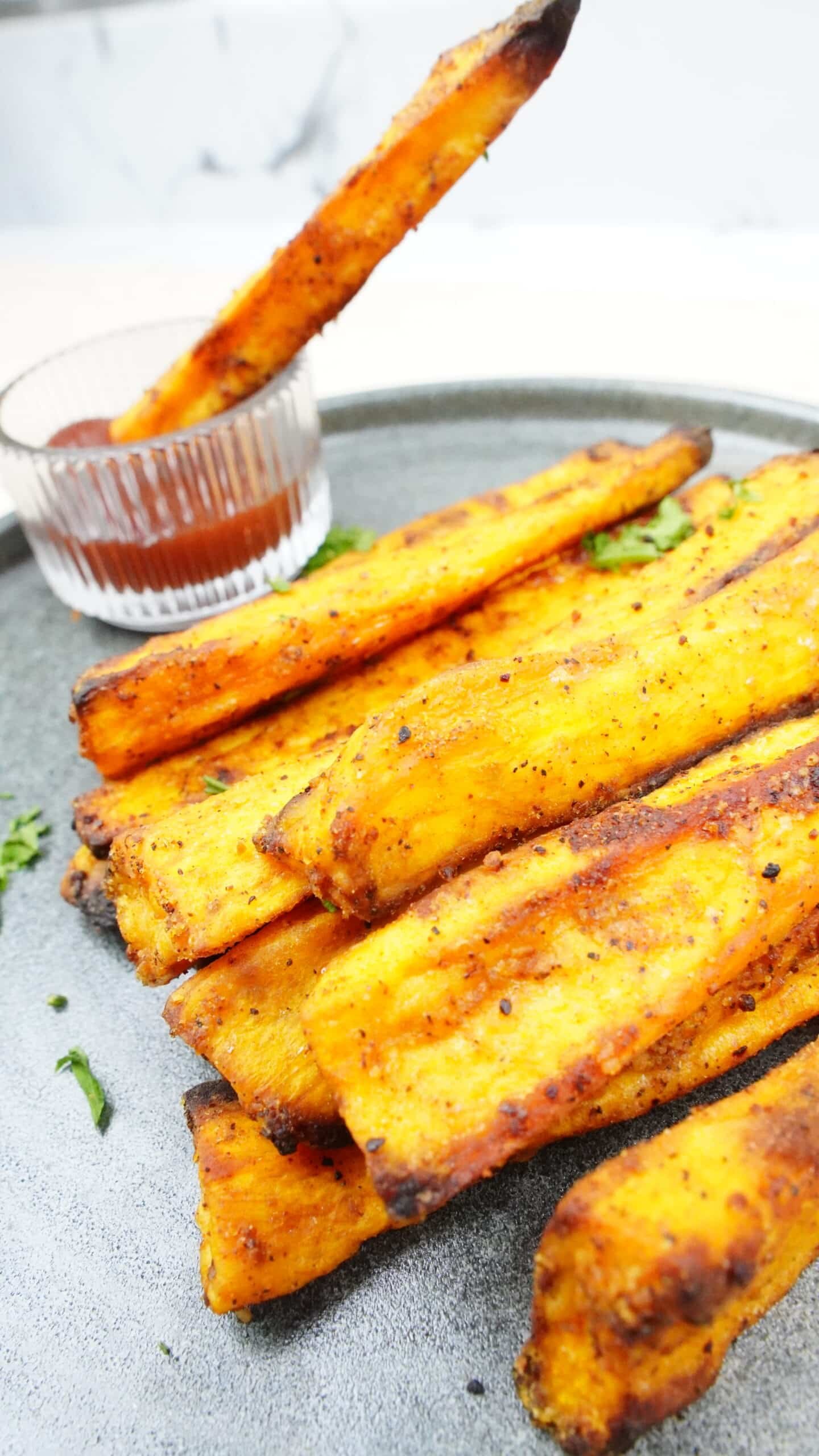 Sweet potato fry being dipped into ketchup beside a tray of fries