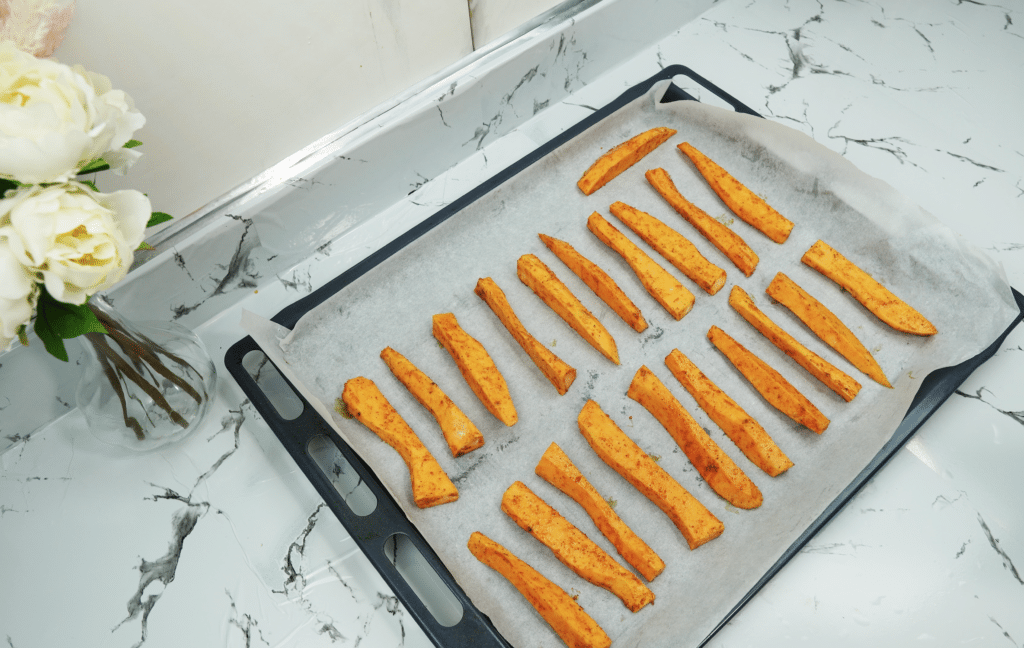 Seasoned sweet potato fries arranged on a parchment-lined sheet pan