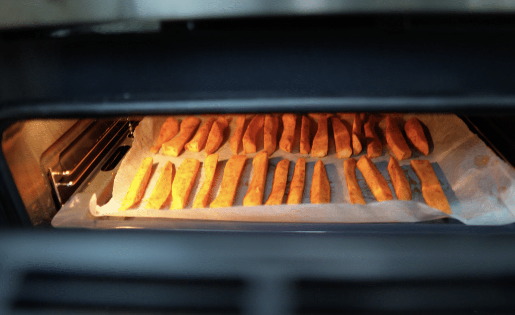 Sweet potato fries baking in the oven on a parchment-lined tray