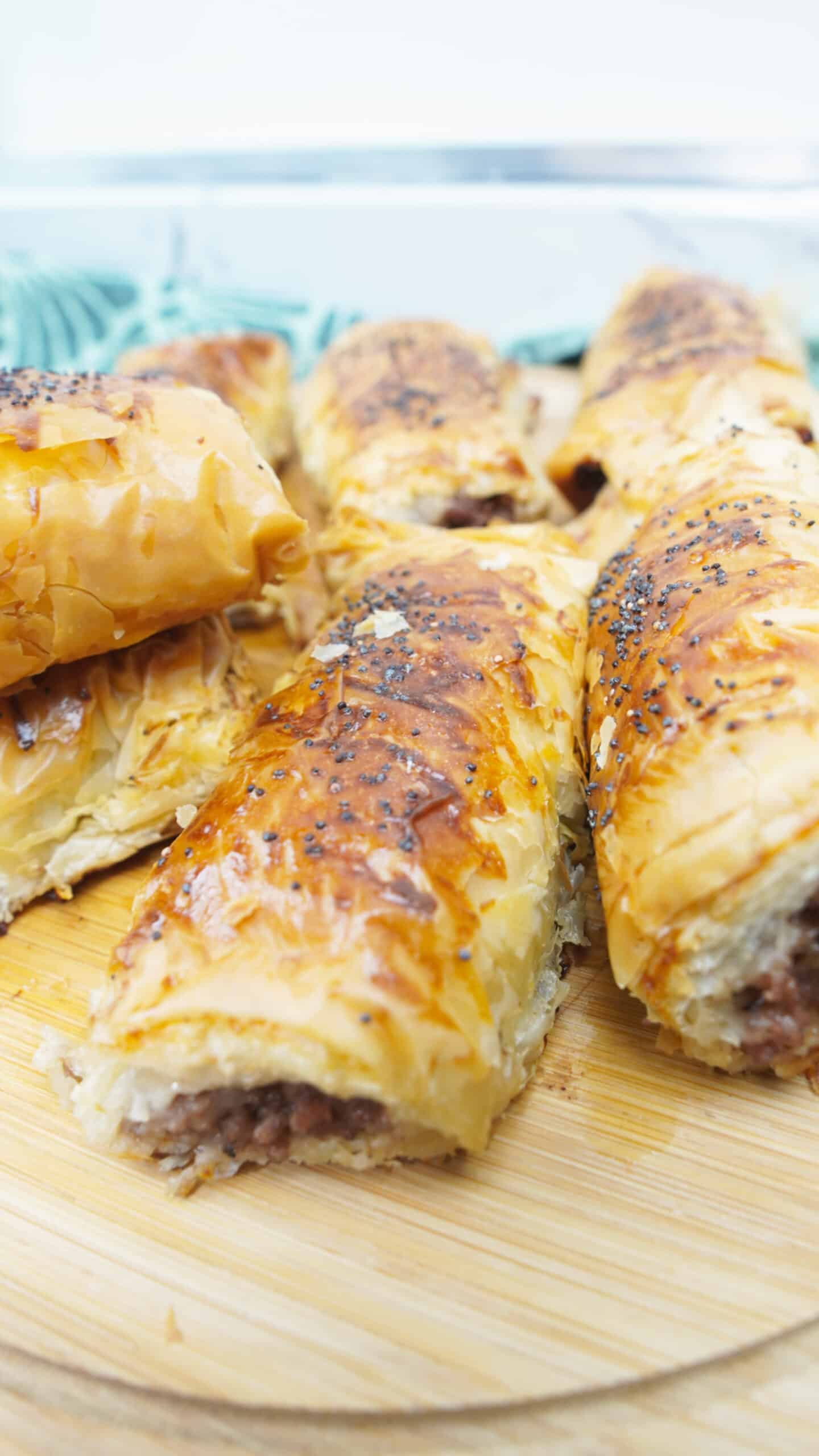 Hand holding a crispy minced meat cigar with poppy seeds on top