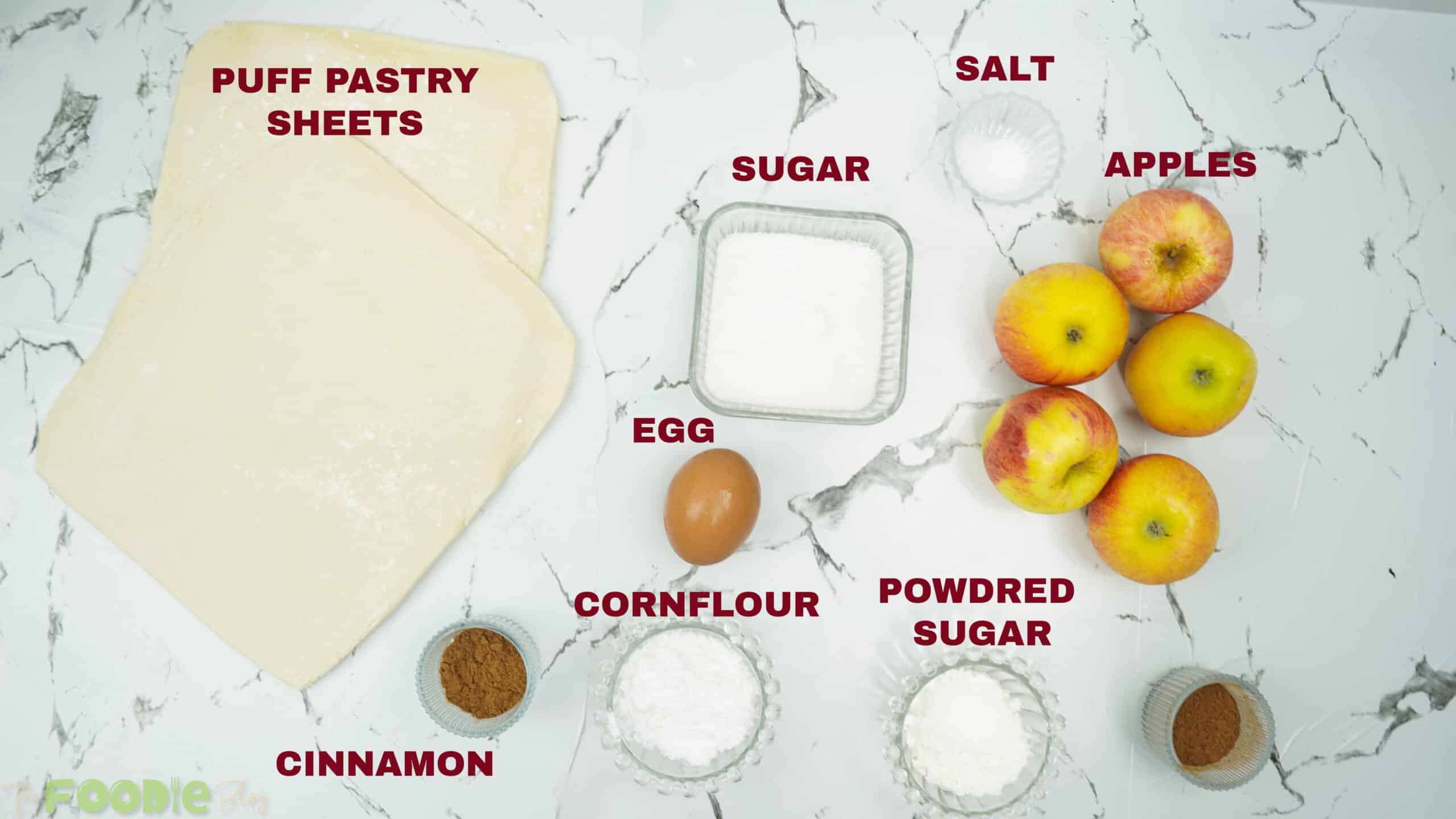 Puff pastry sheets, apples, sugar, cinnamon, cornstarch, egg, and powdered sugar on a counter