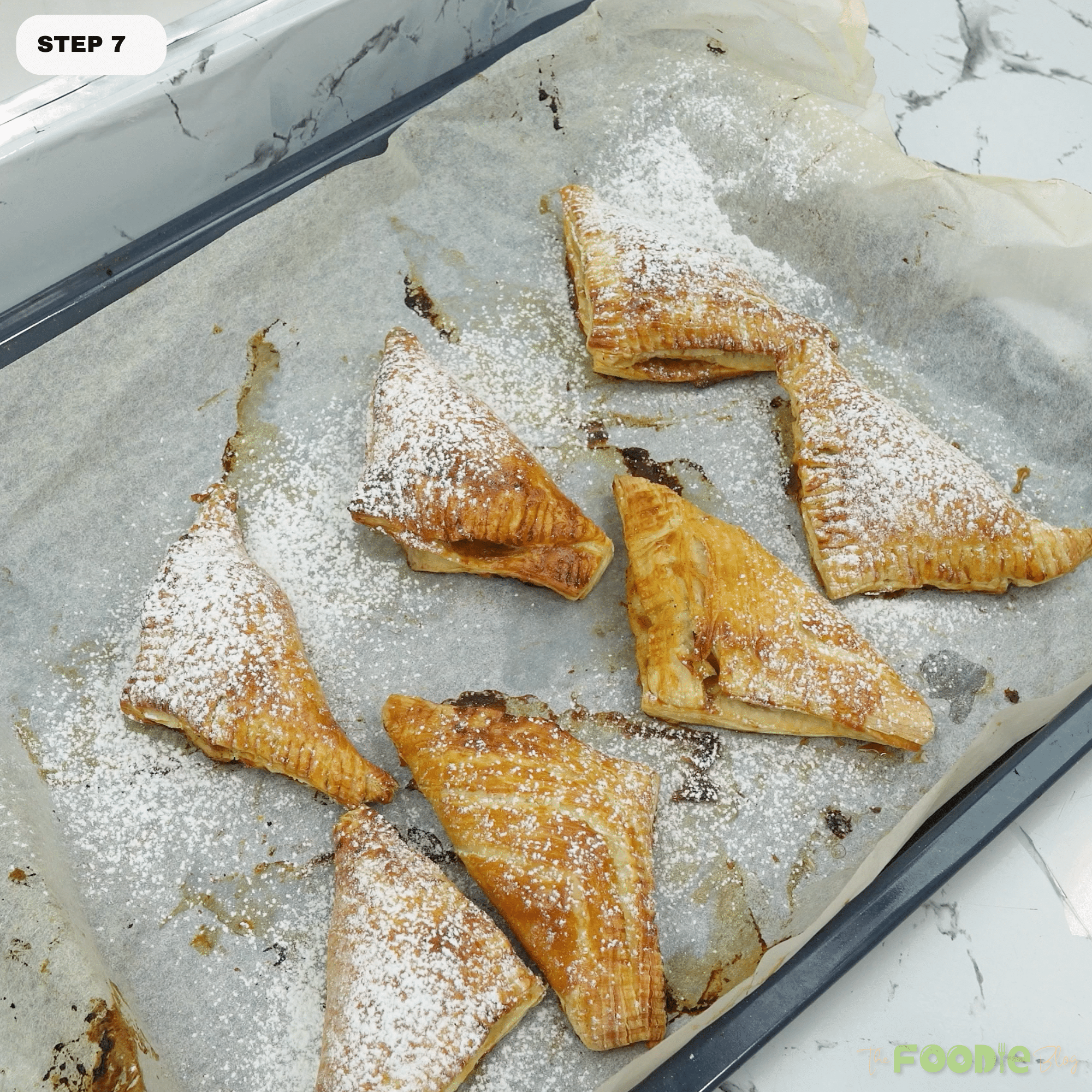 Baked apple turnovers dusted with powdered sugar on a parchment-lined tray
