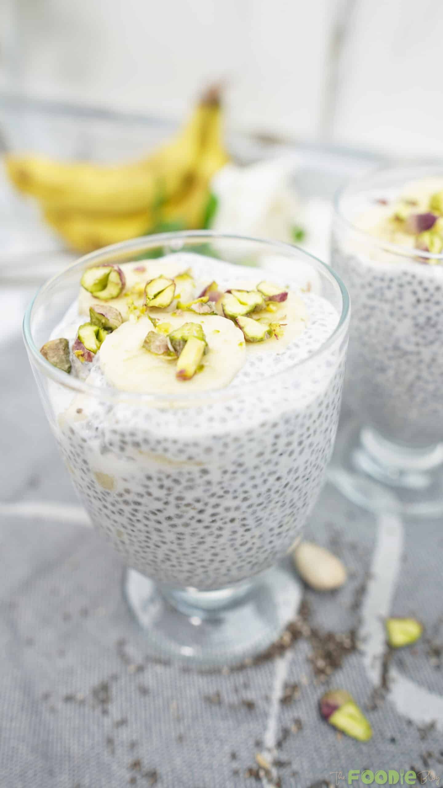 Close-up of chia pudding in a glass topped with banana slices and sliced pistachios.
