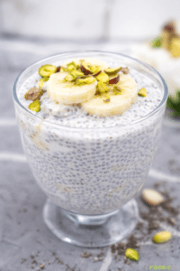 Banana chia seed pudding in a glass cup topped with banana slices and pistachios.