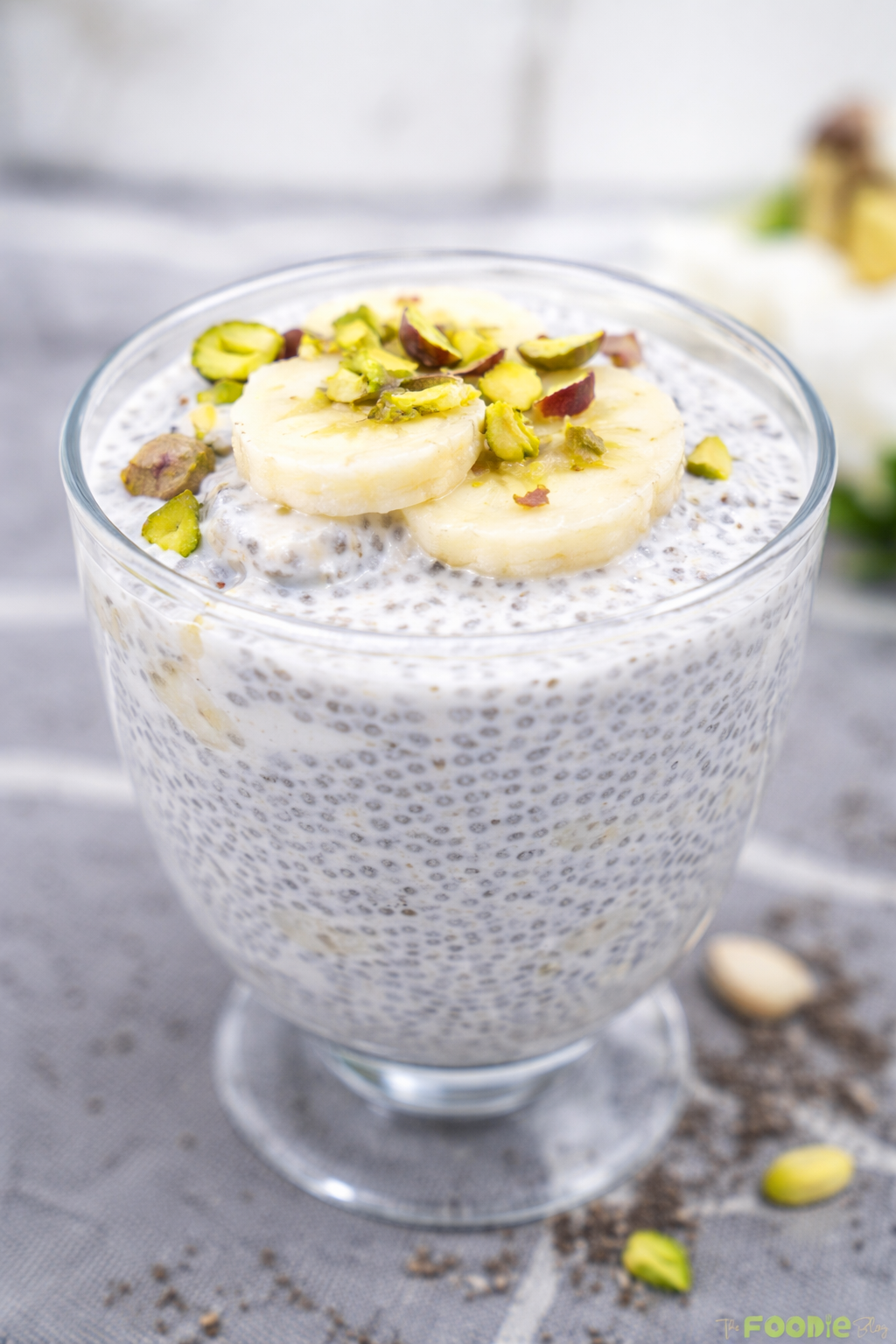 Banana chia seed pudding in a glass cup topped with banana slices and pistachios.