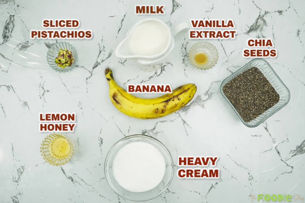 Ingredients for banana chia seed pudding including banana, chia seeds, milk, vanilla, heavy cream, lemon honey, and pistachios.