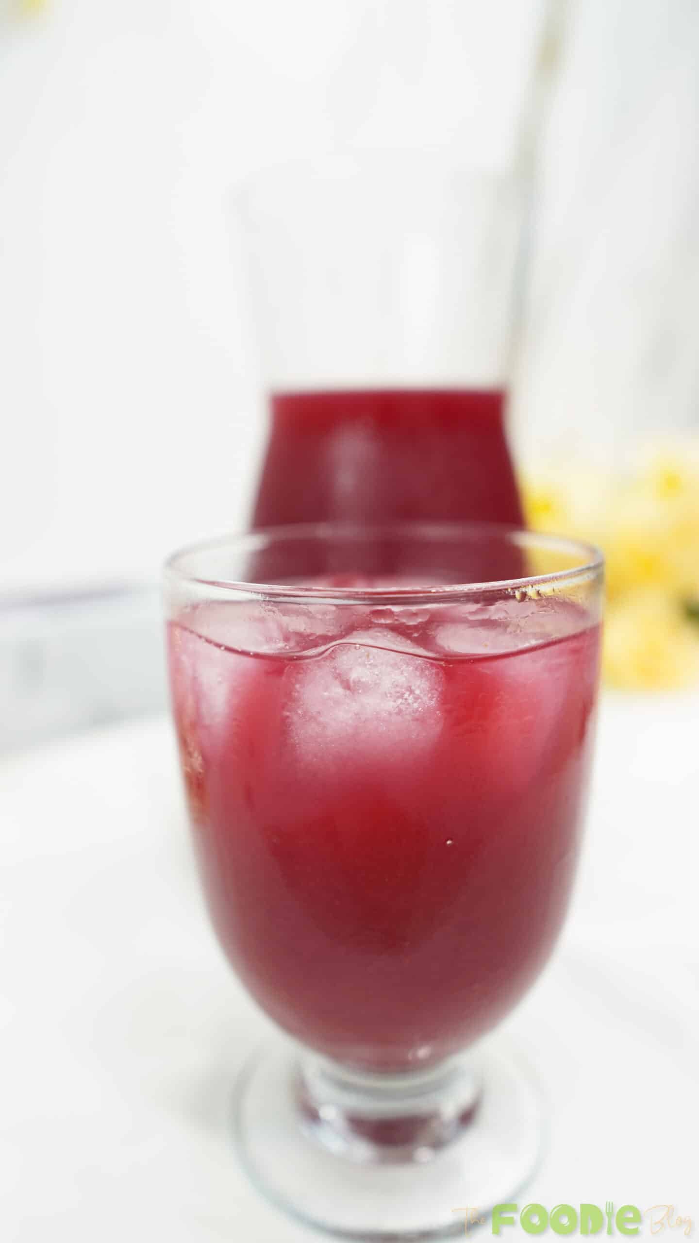 Close-up of a glass filled with beetroot juice and ice cubes on a bright background