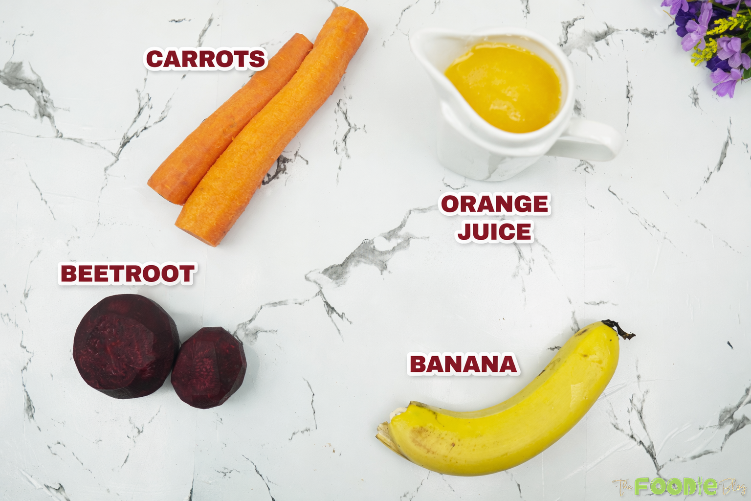 Ingredients for beetroot juice: beetroot, carrots, banana, and orange juice on a marble background.