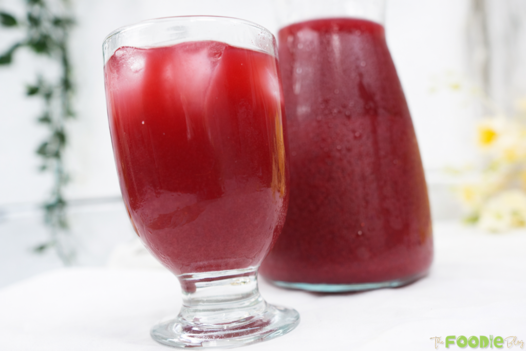 Glass of beetroot juice over ice with a chilled beetroot juice carafe in the background.