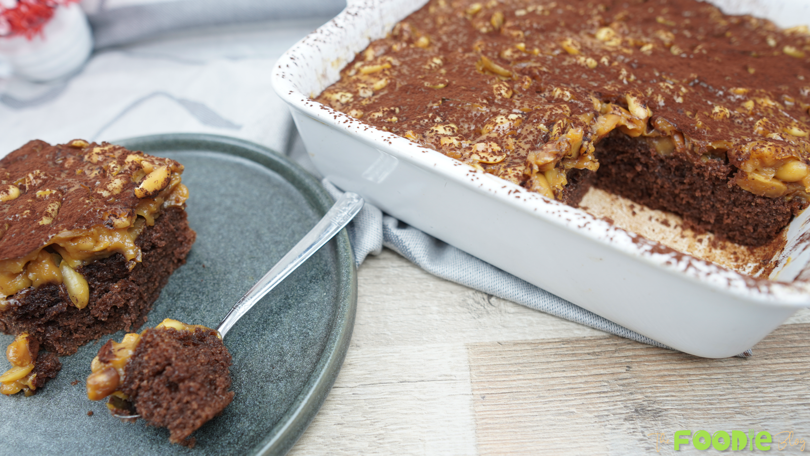 Chocolate cake with caramel peanut topping in a white baking dish with a slice served