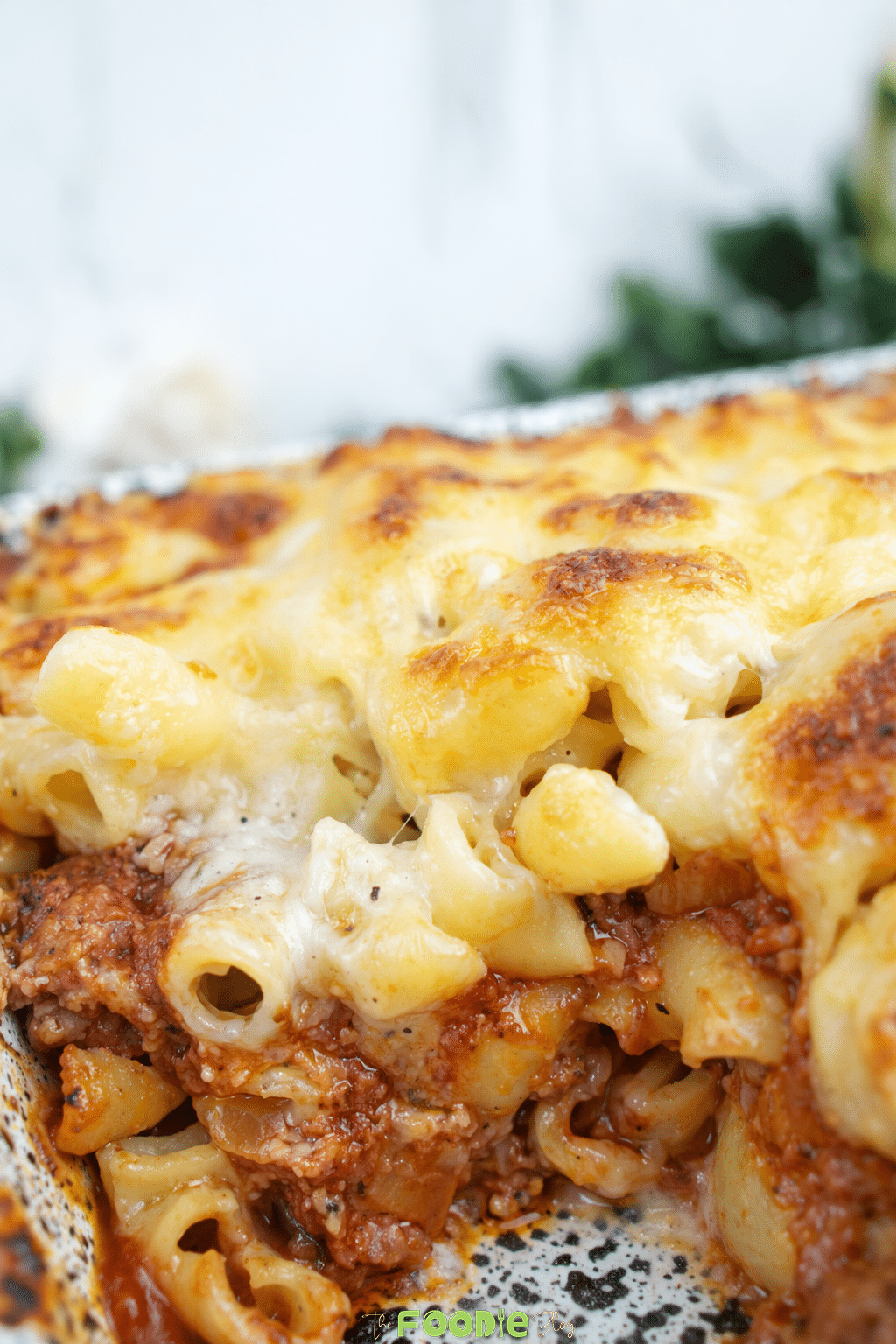 Served portion of cheese meat pasta bake on a black plate with melted cheese, beef sauce, and pasta.