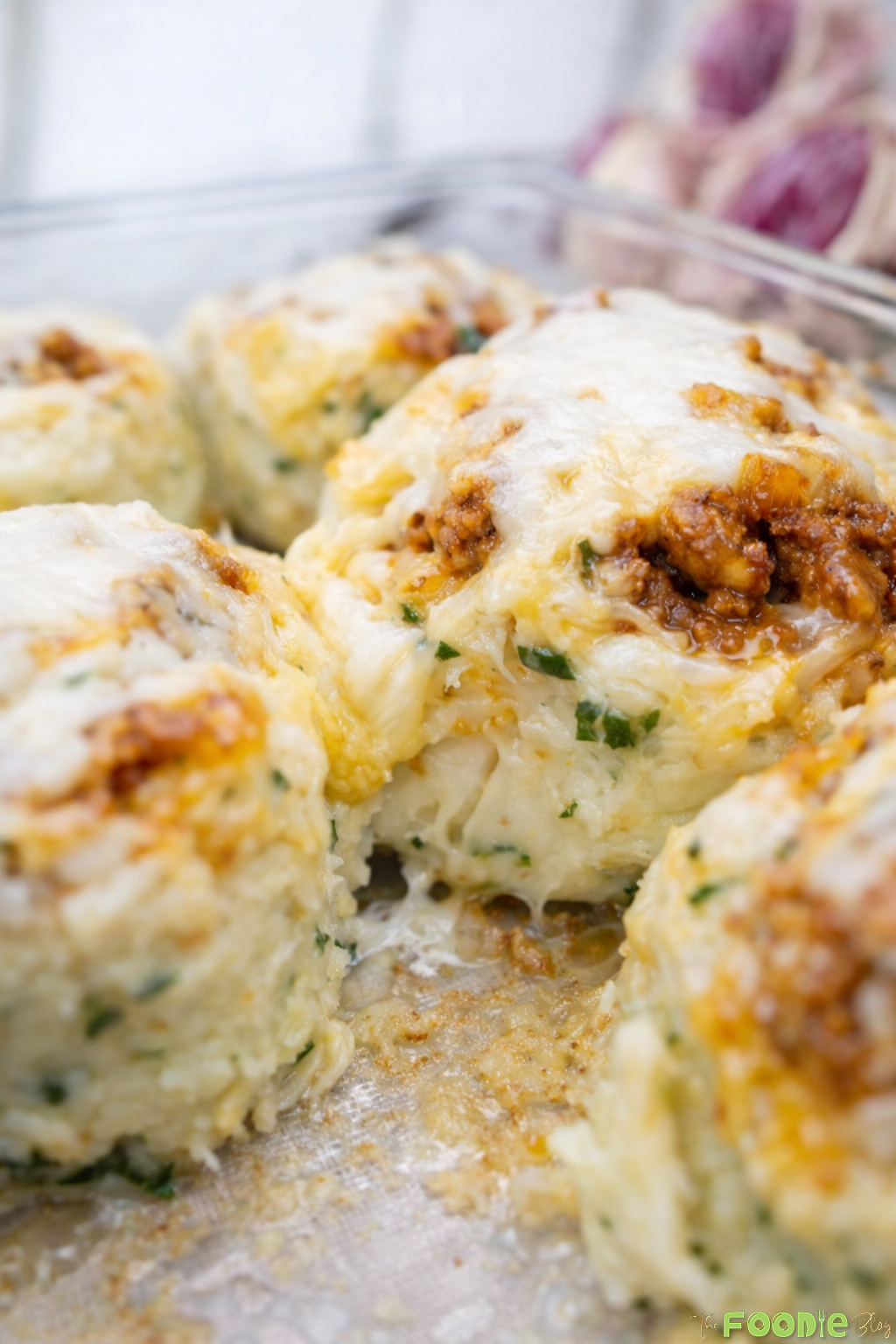 Cheesy beef potato balls baked in a dish with melted cheese on top.